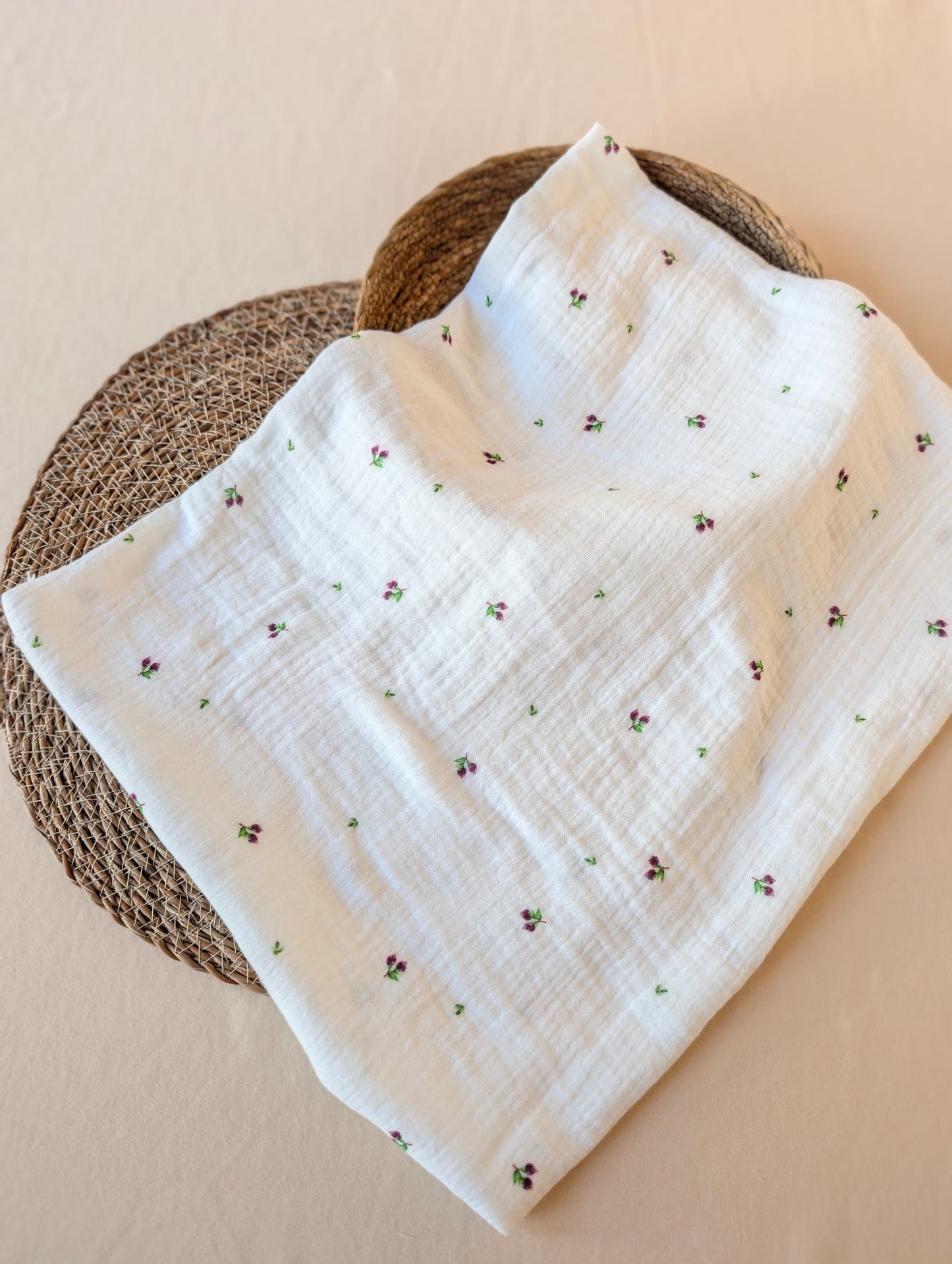 Double gauze Mini Blueberries fabric folded on rattan showing soft texture and scattered berry and leaf print on white