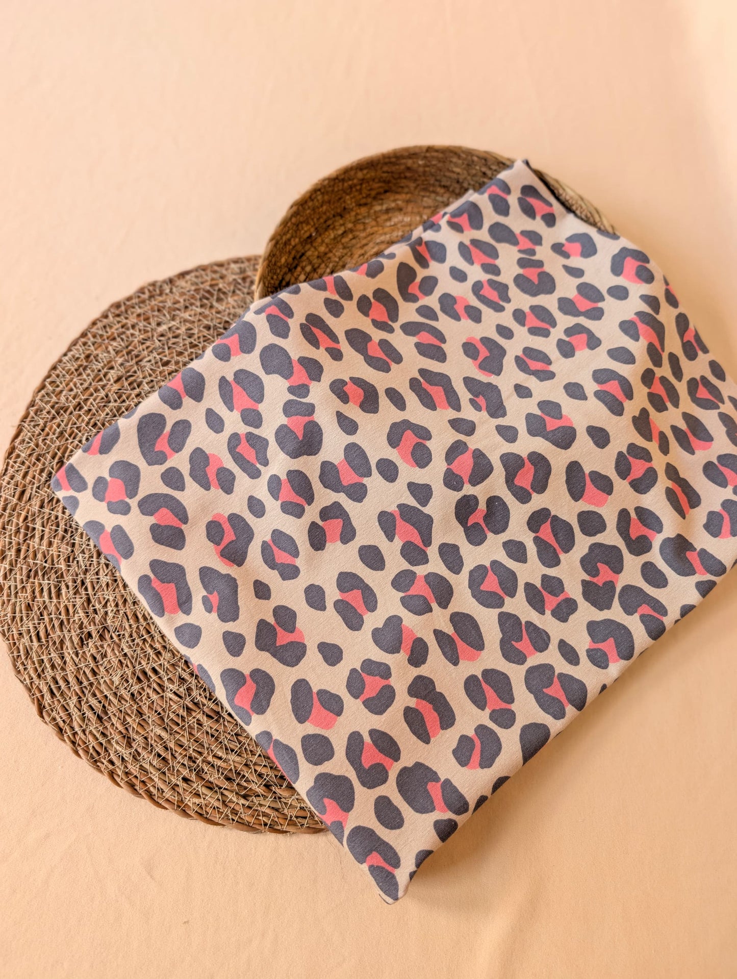 Natural ground cotton jersey folded flat on wicker showing the full Nala Animal Print — bold slate and coral leopard spots — by Esorai