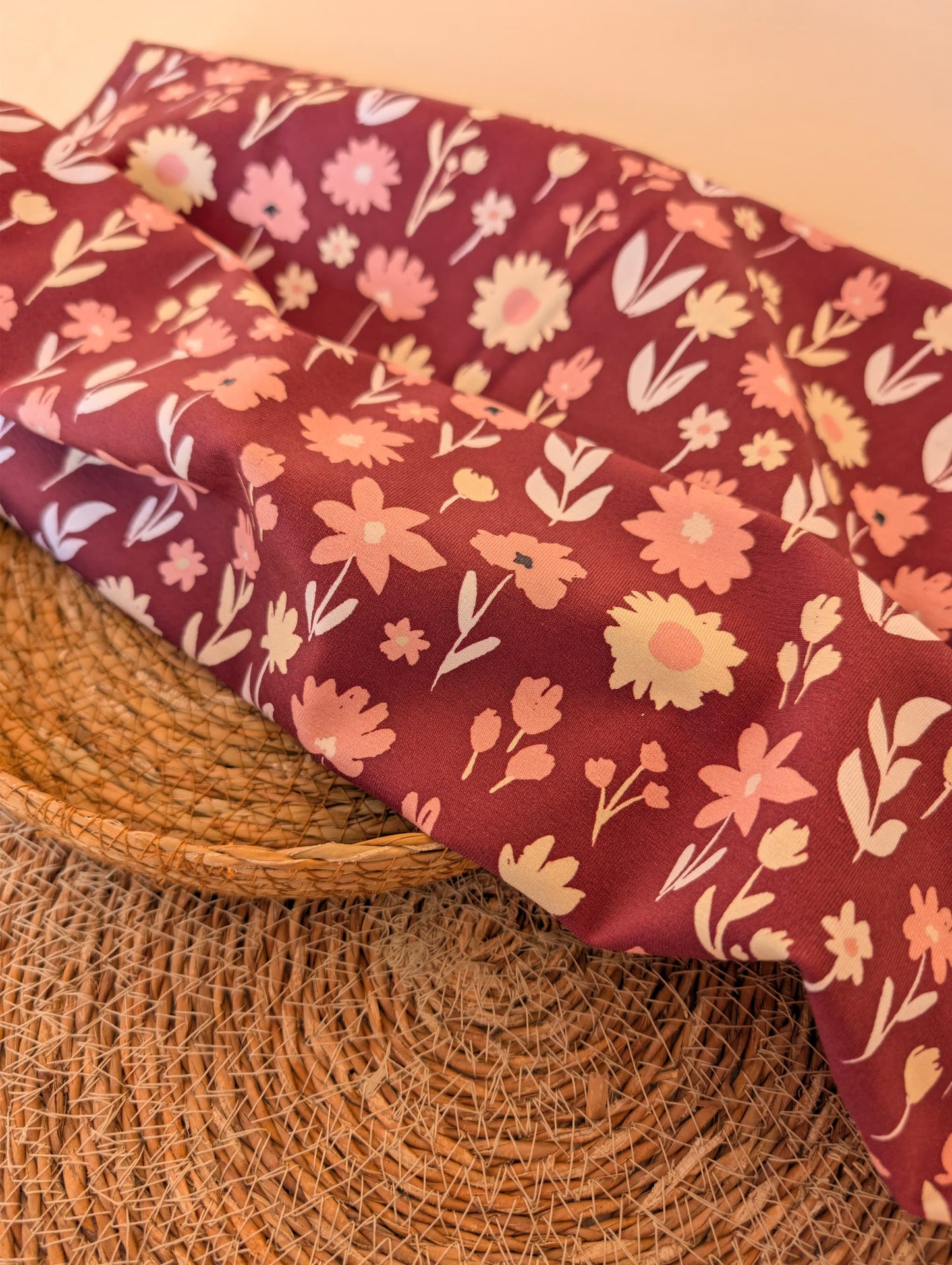 Ottie Floral cotton jersey draped over a wicker basket — scattered daisy and tulip print in pink and cream on a deep burgundy ground — Esorai