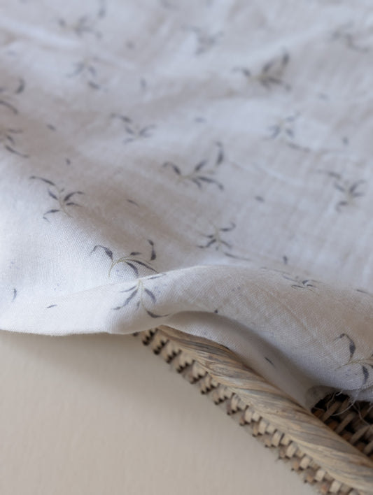 Close-up of double gauze fabric folded over a rattan basket edge showing Winnie leaf sprig print detail and soft crinkle texture