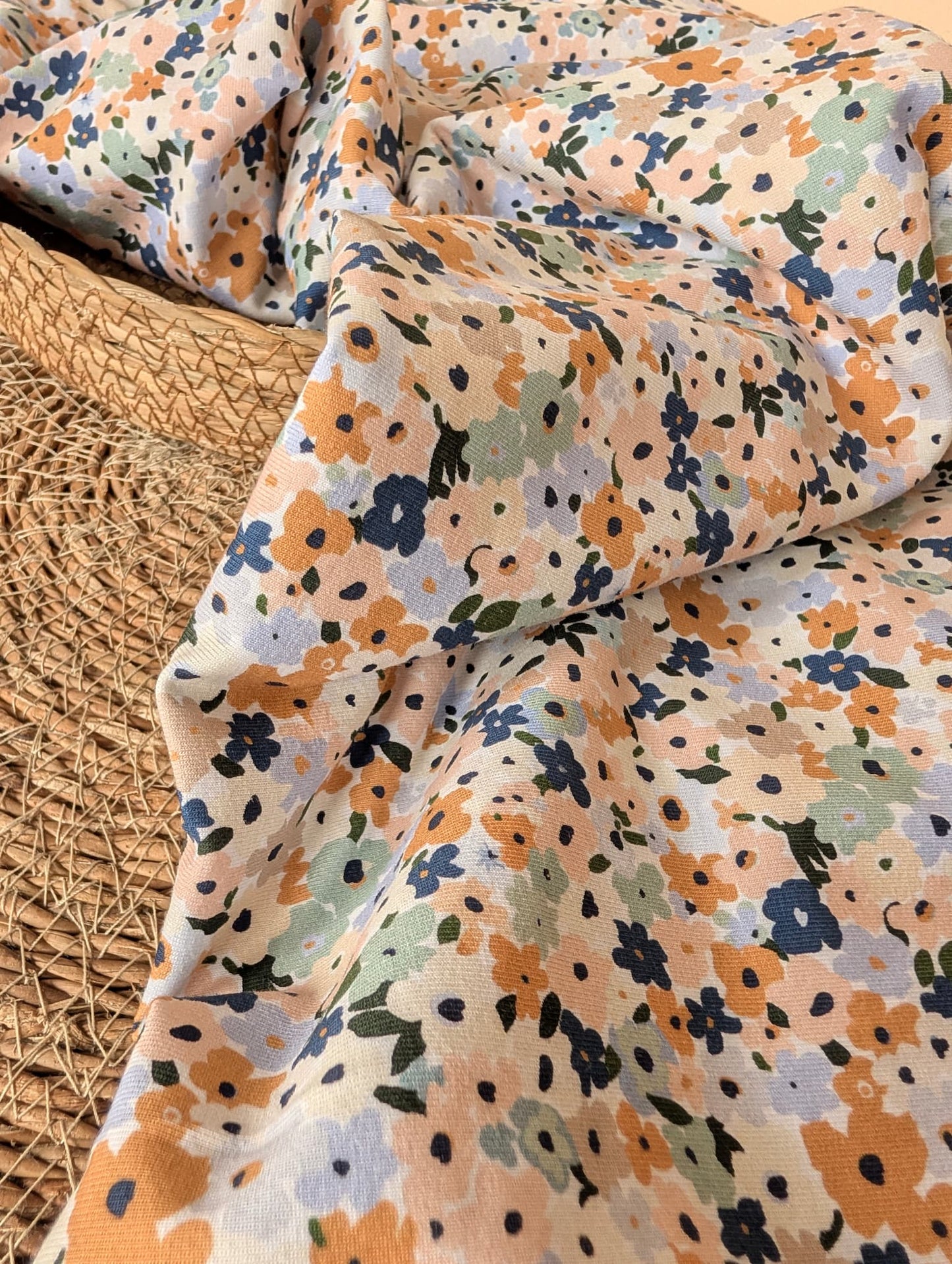 Cotton jersey fabric folded on a rattan placemat — Brooke Floral pastel multi ditsy floral print on white cotton jersey