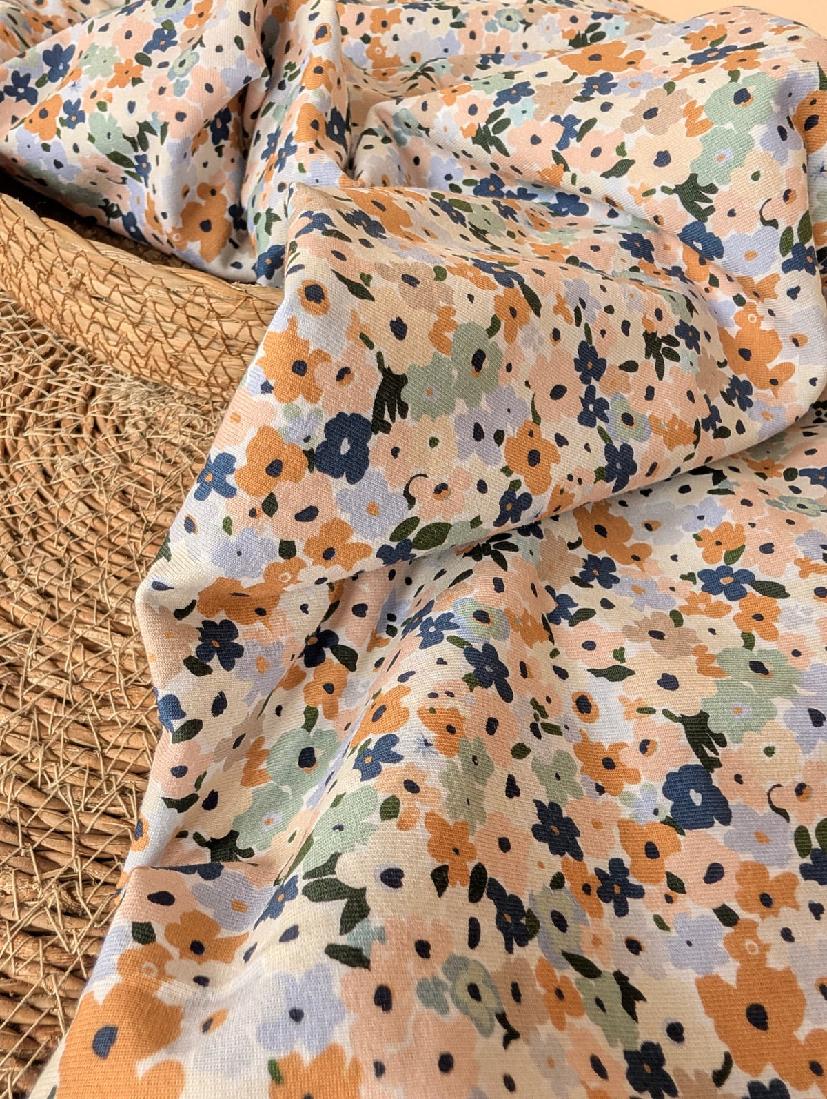 Cotton jersey fabric folded on a rattan placemat — Brooke Floral pastel multi ditsy floral print on white cotton jersey