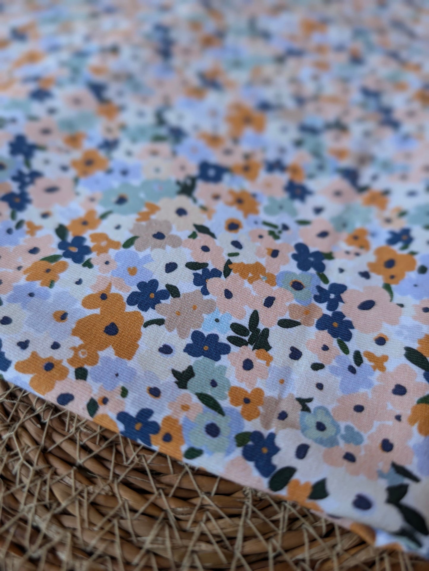 Cotton jersey fabric folded on a rattan placemat — Brooke Floral pastel multi ditsy floral print on white cotton jersey