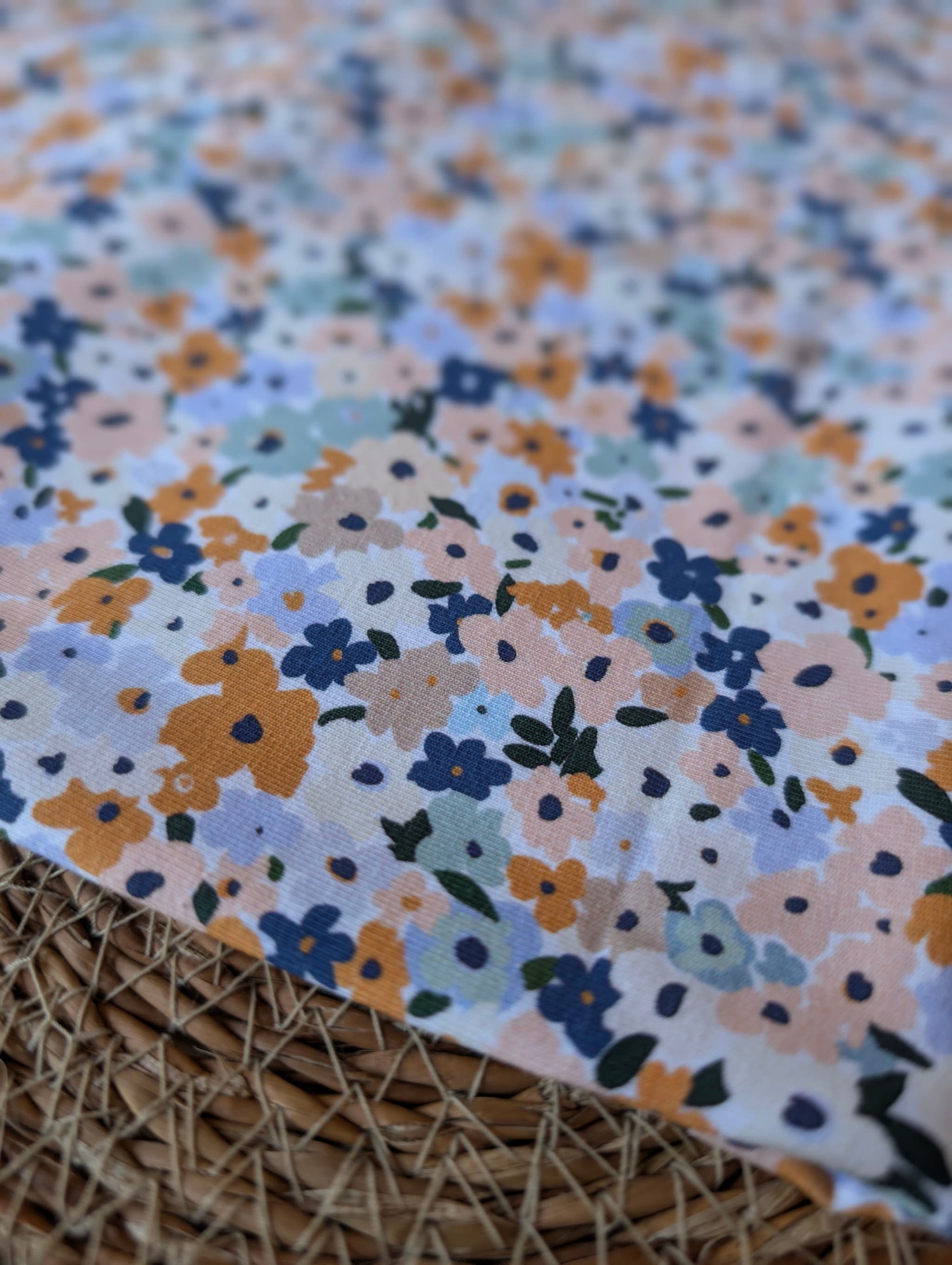 Cotton jersey fabric folded on a rattan placemat — Brooke Floral pastel multi ditsy floral print on white cotton jersey