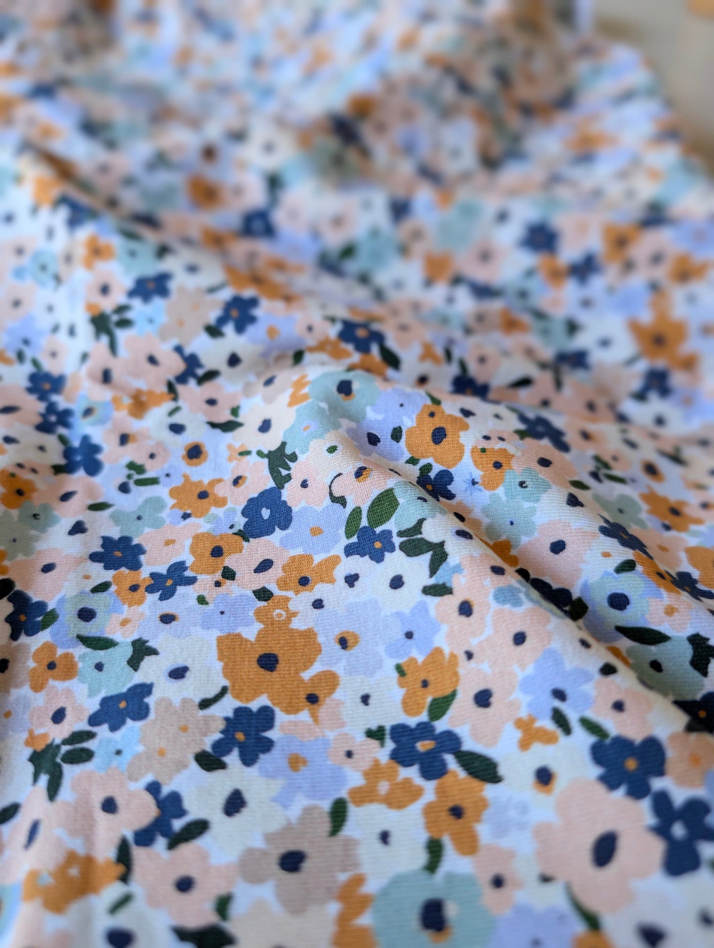 Close-up of cotton jersey fabric showing wildflower ditsy florals — Brooke Floral in peach, dusty blue, mustard and sage on white
