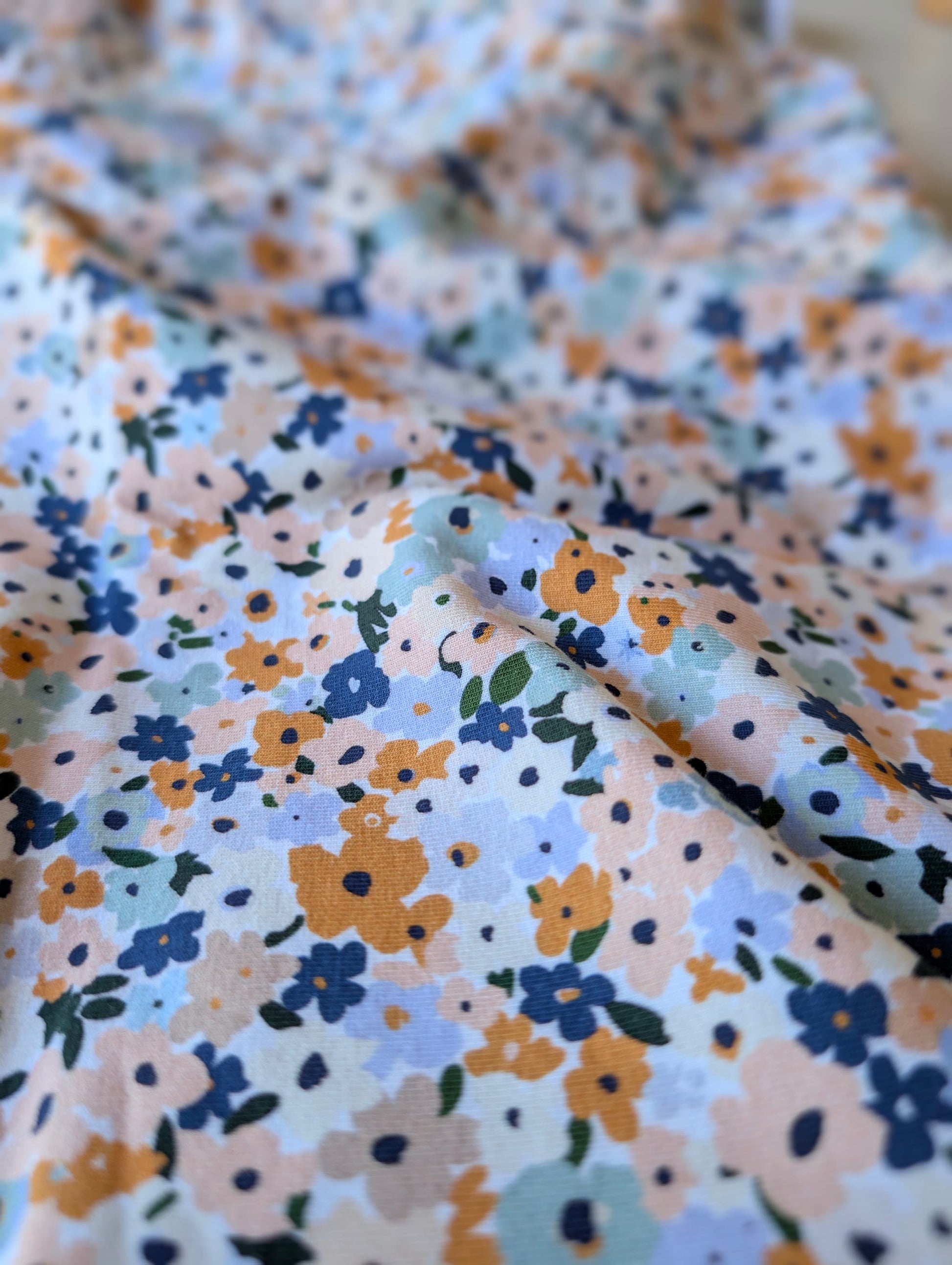 Close-up of cotton jersey fabric showing wildflower ditsy florals — Brooke Floral in peach, dusty blue, mustard and sage on white