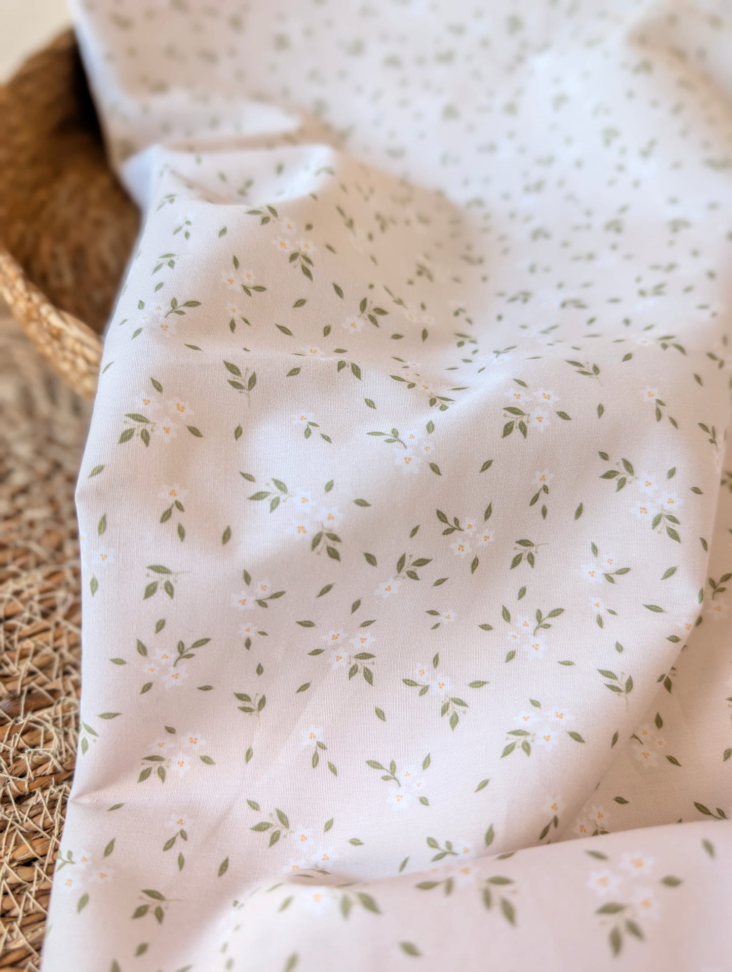 Clemmie Ditsy Floral Cotton Poplin by esorai — scattered green leaf and white blossom print on white ground, fabric draped in wicker basket