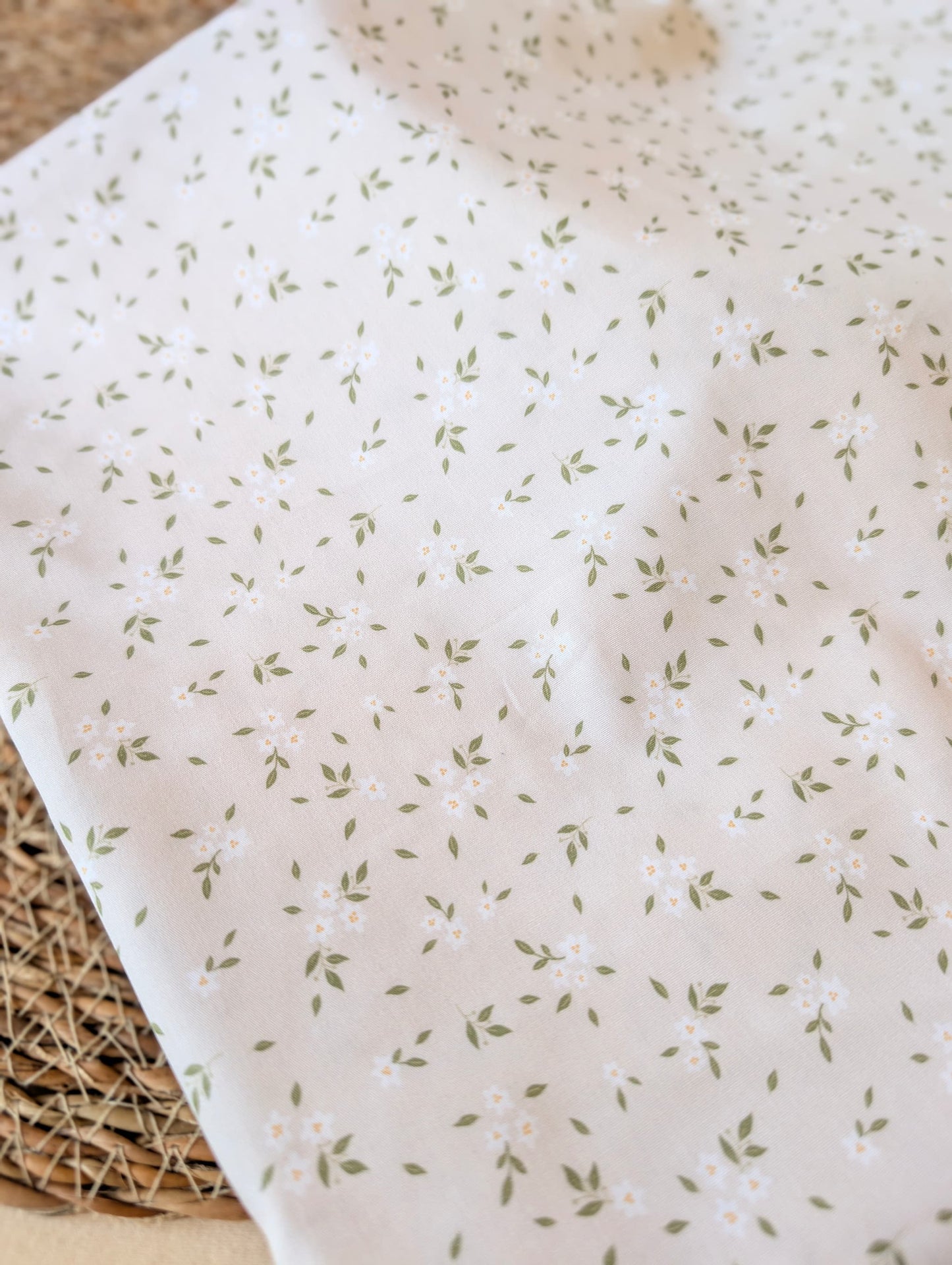 Clemmie Ditsy Floral Cotton Poplin by esorai — scattered green leaf and white blossom print on white ground, fabric draped in wicker basket
