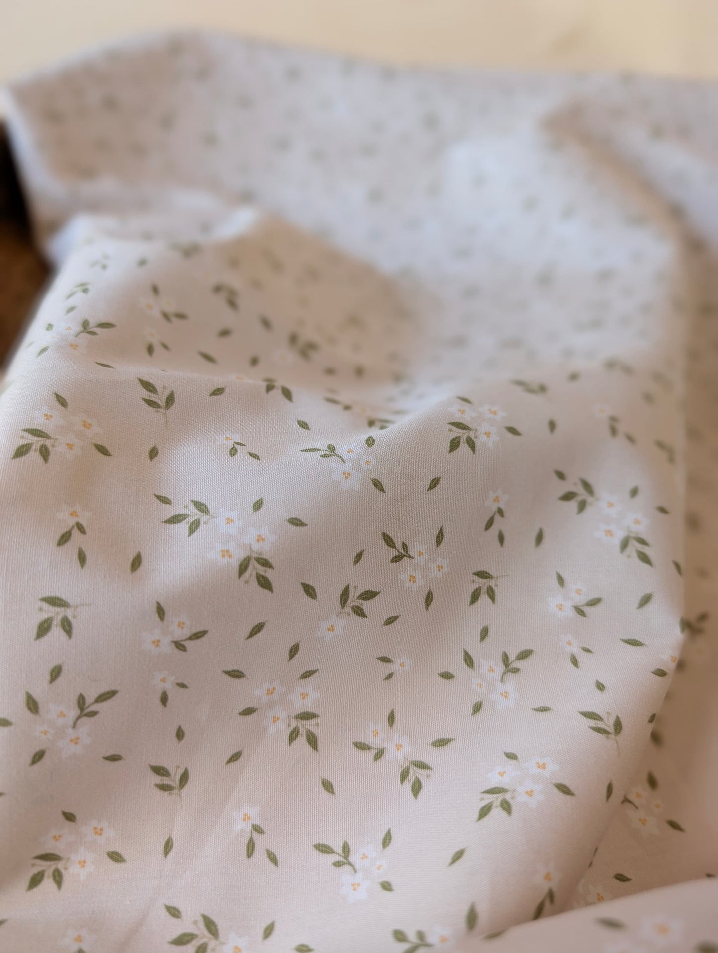 Clemmie Ditsy Floral Cotton Poplin by esorai — scattered green leaf and white blossom print on white ground, fabric draped in wicker basket