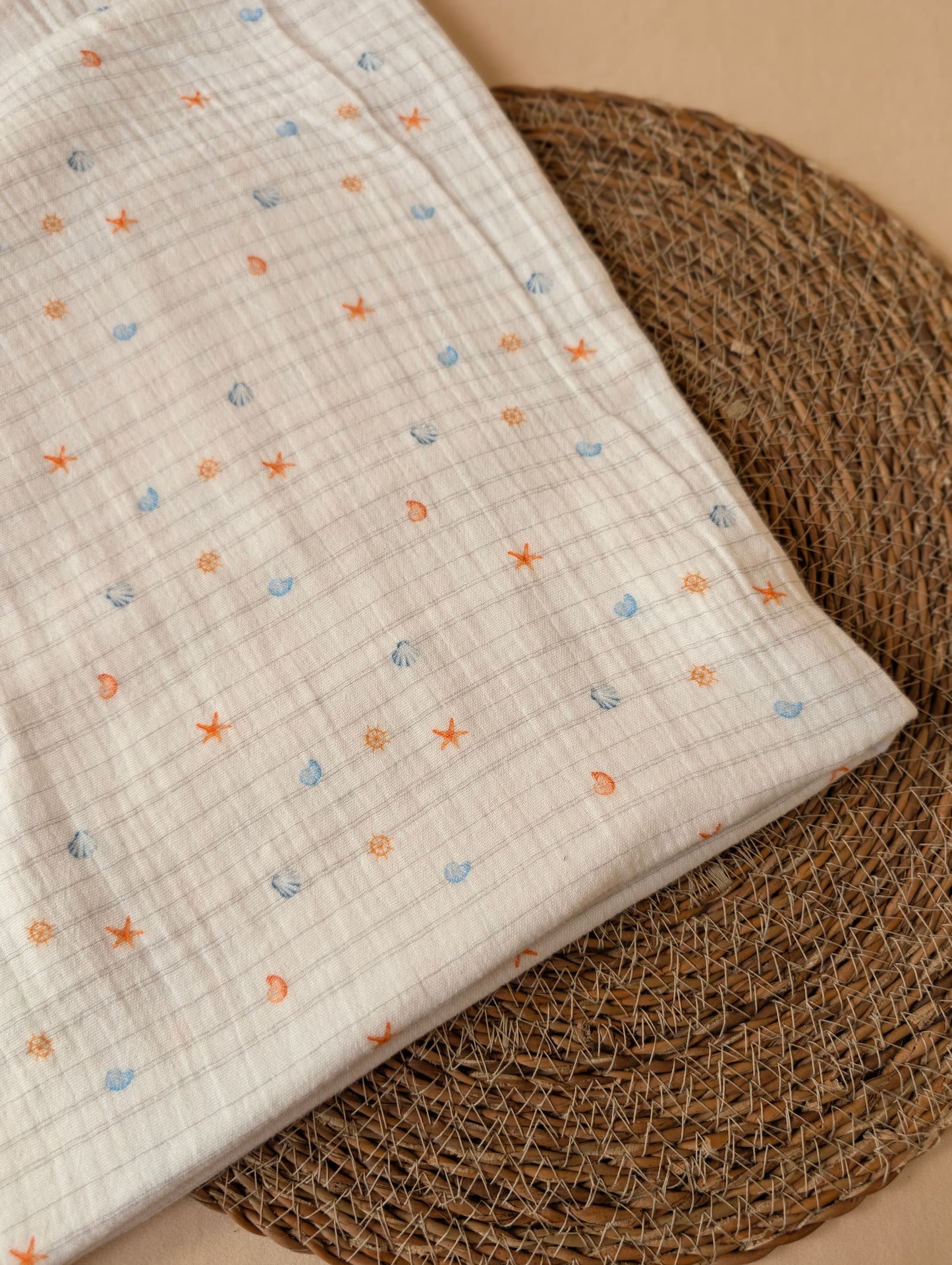 Close-up of white double gauze showing Cora Coastal print detail — miniature scallop shells, starfish and nautical wheel motifs in coral orange and blue — Esorai