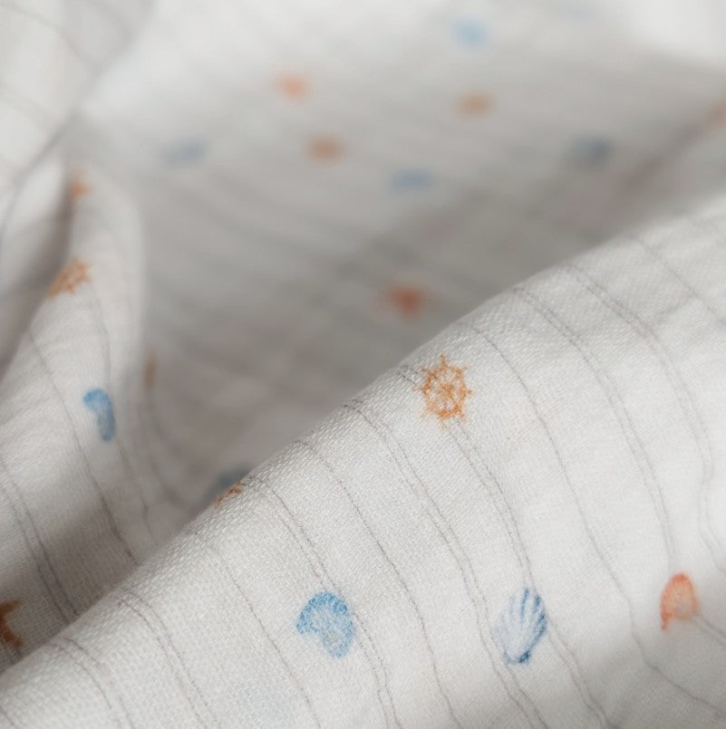 White double gauze fabric close-up showing woven grid texture with scattered tiny starfish and seashells in coral orange and dusty blue — Cora Coastal double gauze by Esorai