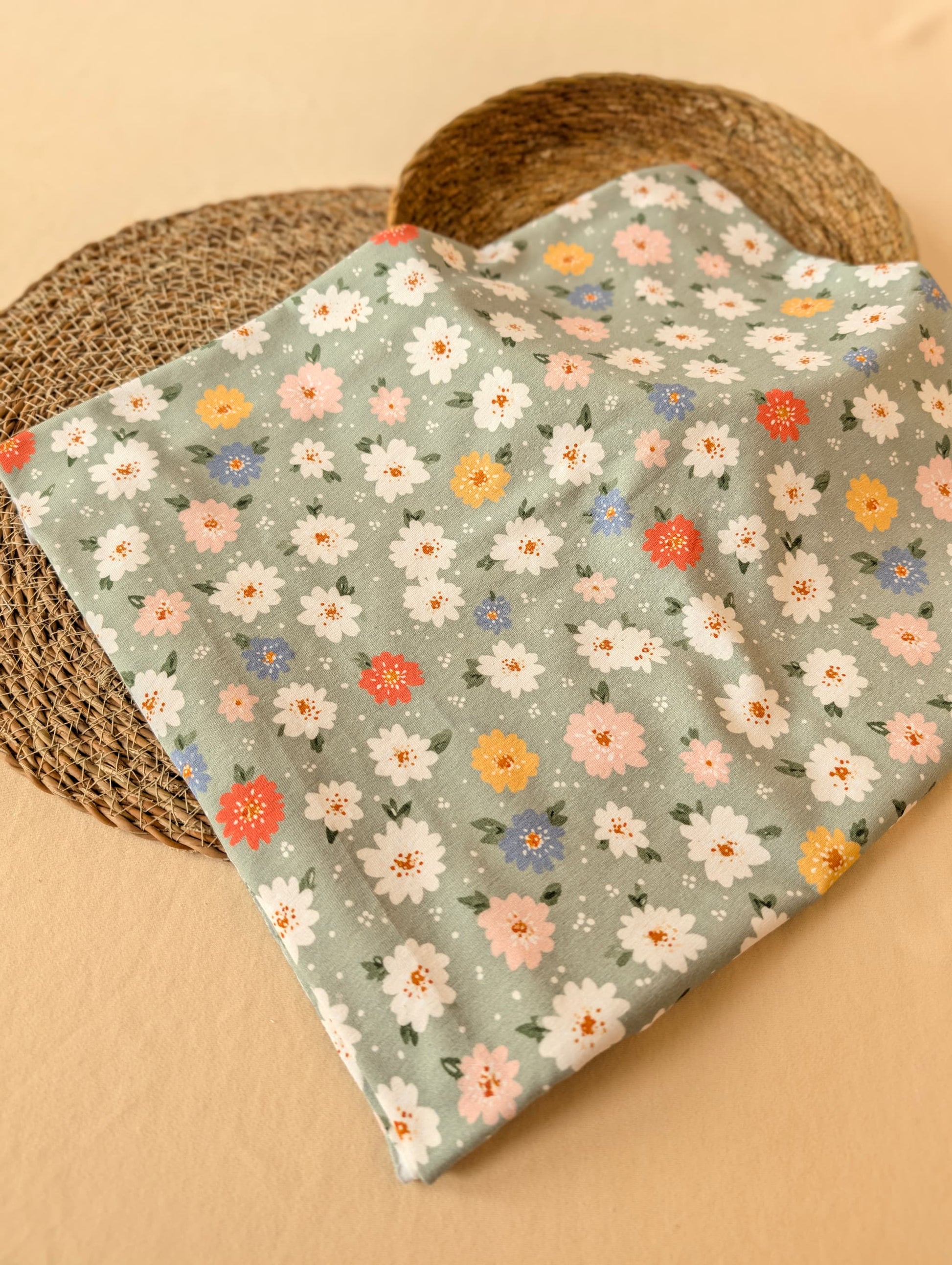 Daisy Floral Cotton Jersey in Sage folded flat on wicker mat — daisy print in warm neutral tones on muted sage green cotton jersey — Esorai