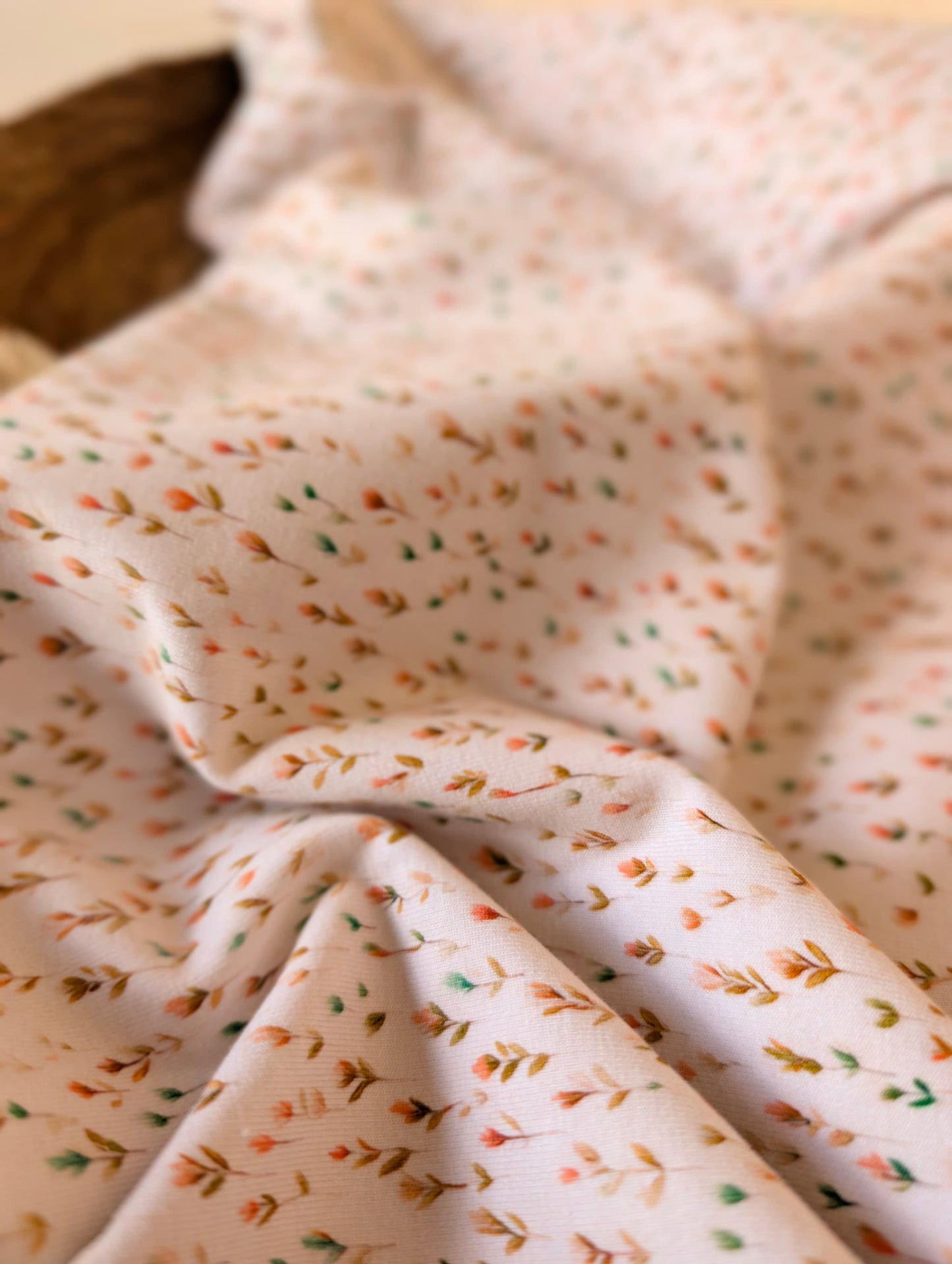 Close-up of cotton jersey fabric showing the delicate Edie Sprig print — tiny botanical sprigs in peach, mustard and sage on white