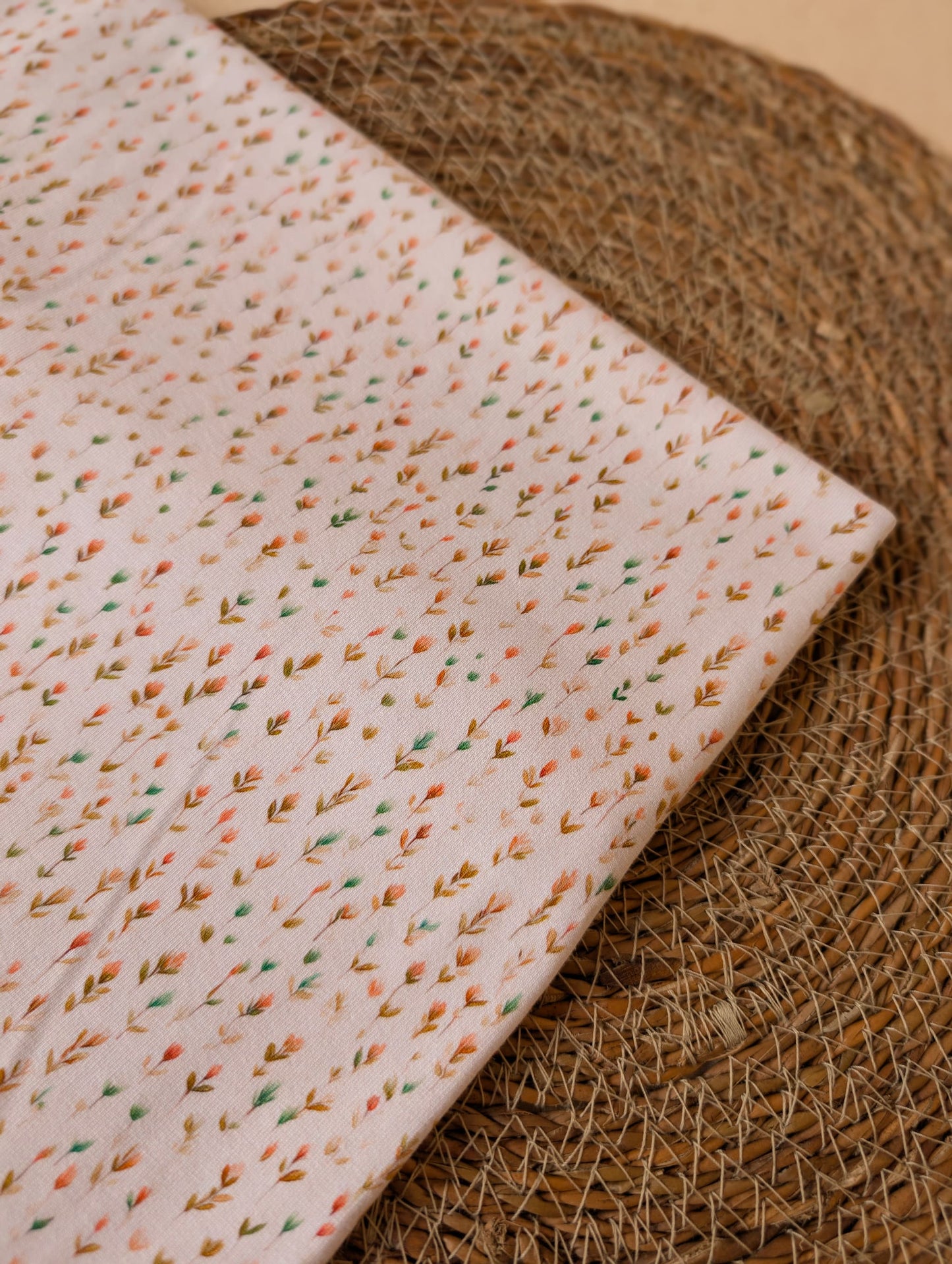 Cotton jersey Edie Sprig fabric folded on a rattan placemat showing the full repeat of the fine scattered sprig print on white