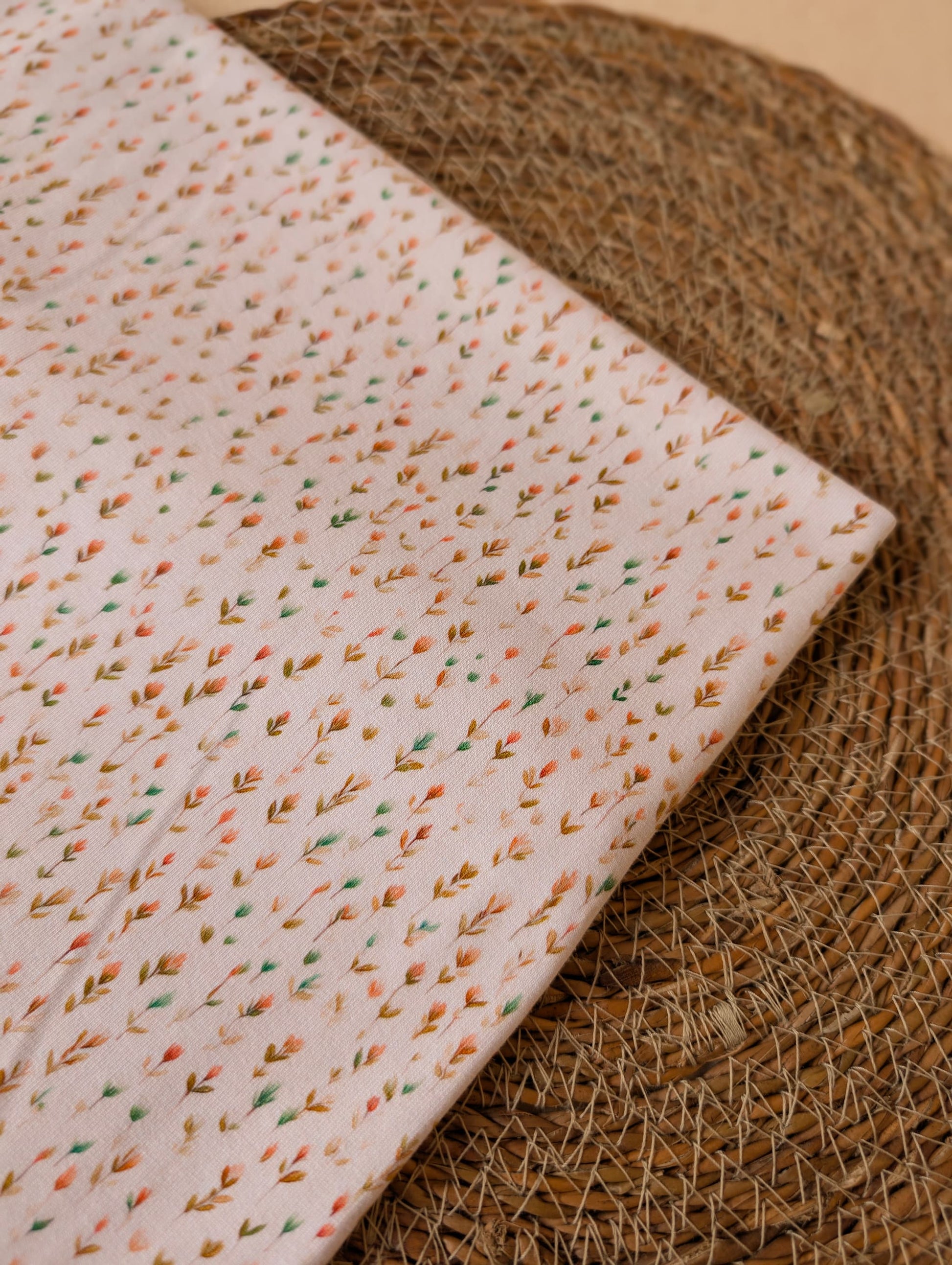 Cotton jersey Edie Sprig fabric folded on a rattan placemat showing the full repeat of the fine scattered sprig print on white