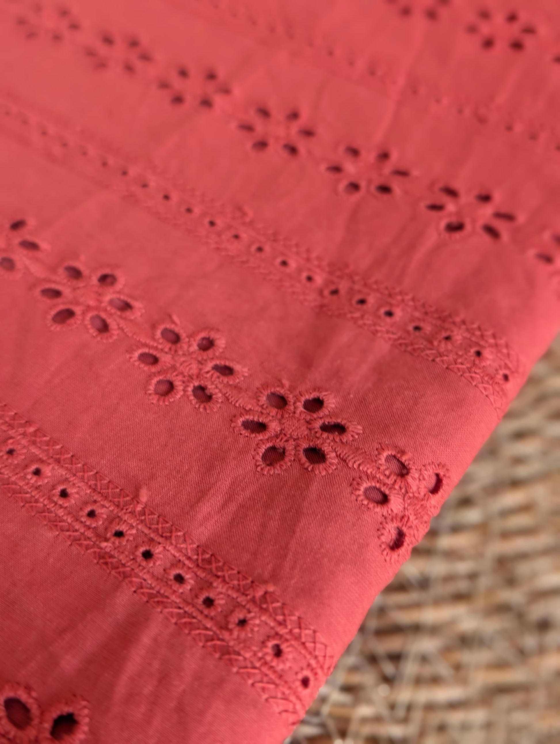 Macro detail of Esme cotton broderie anglaise embroidery, showing individual floral eyelets and ladder-stitch trellis border in rust/terracotta thread