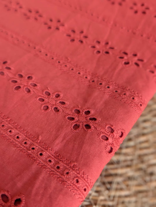 Macro detail of Esme cotton broderie anglaise embroidery, showing individual floral eyelets and ladder-stitch trellis border in rust/terracotta thread