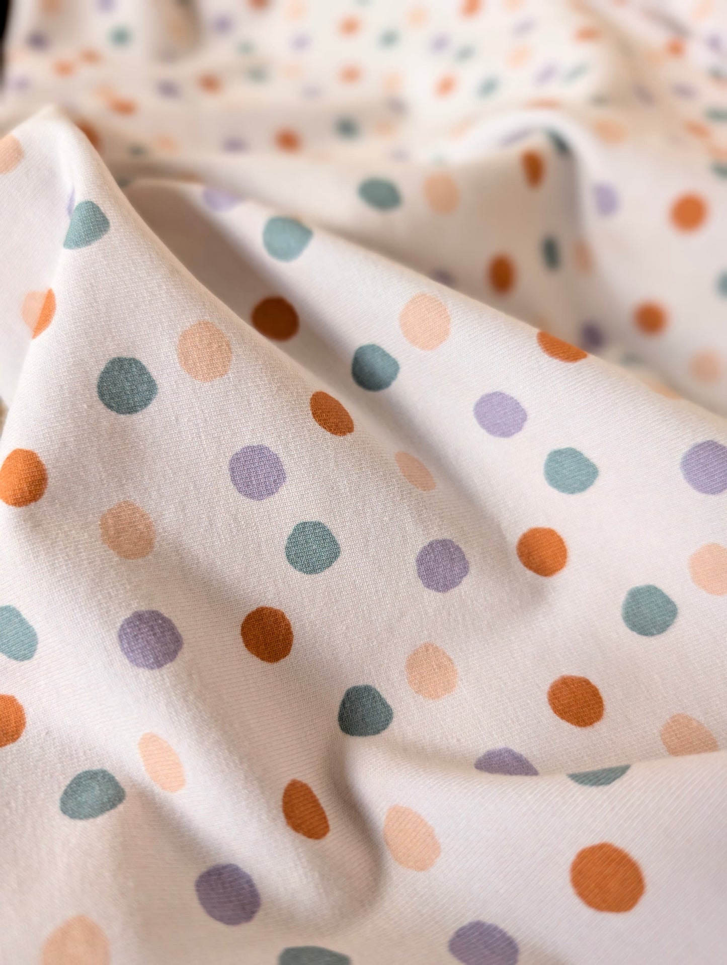 Cotton jersey Etta Spot fabric draped over rattan showing drape and stretch — scattered pastel spots on white