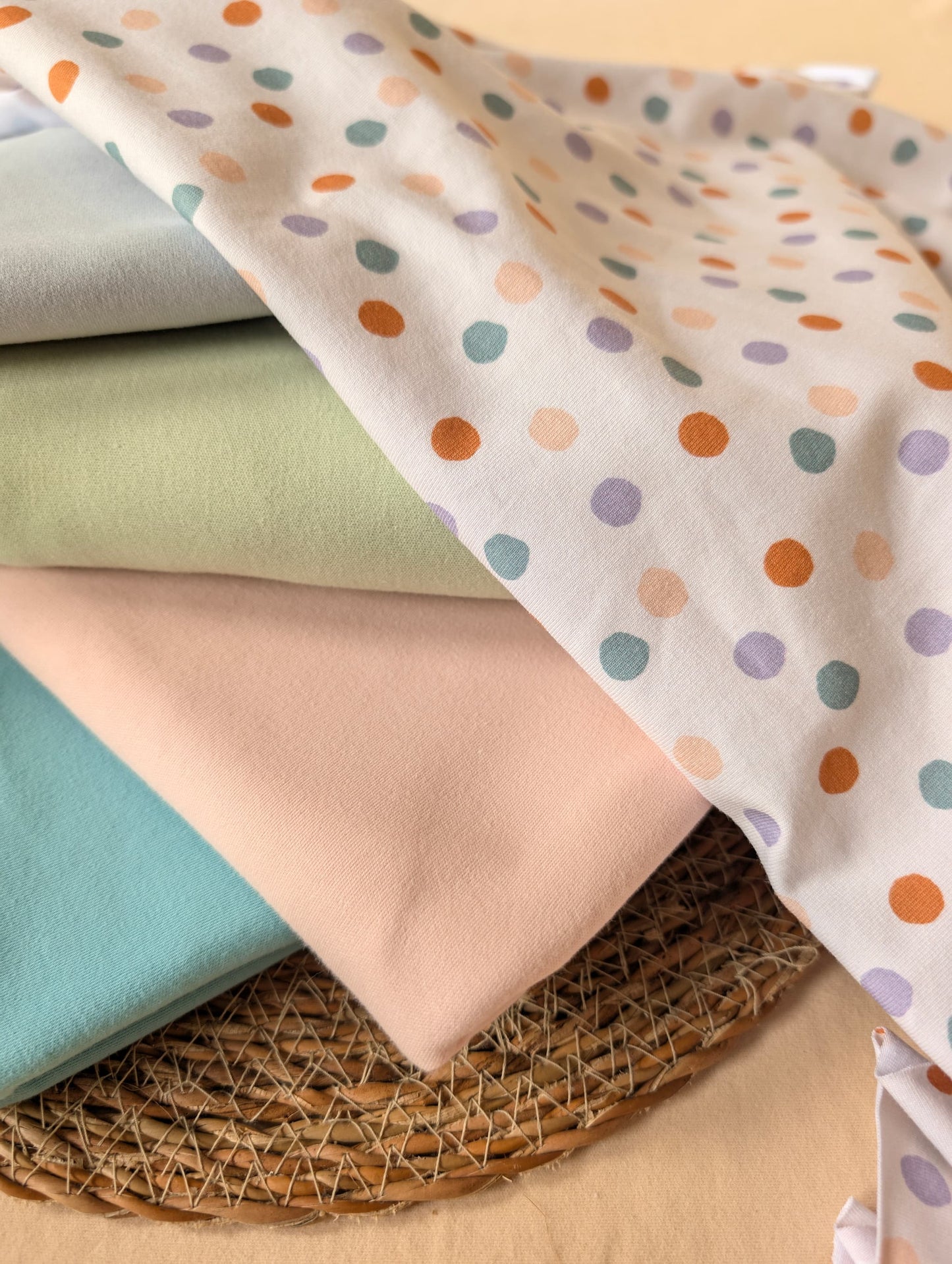 
Cotton jersey Etta Spot fabric stacked with plain cotton jersey in sage, blush and teal — pastel multi scattered spot print