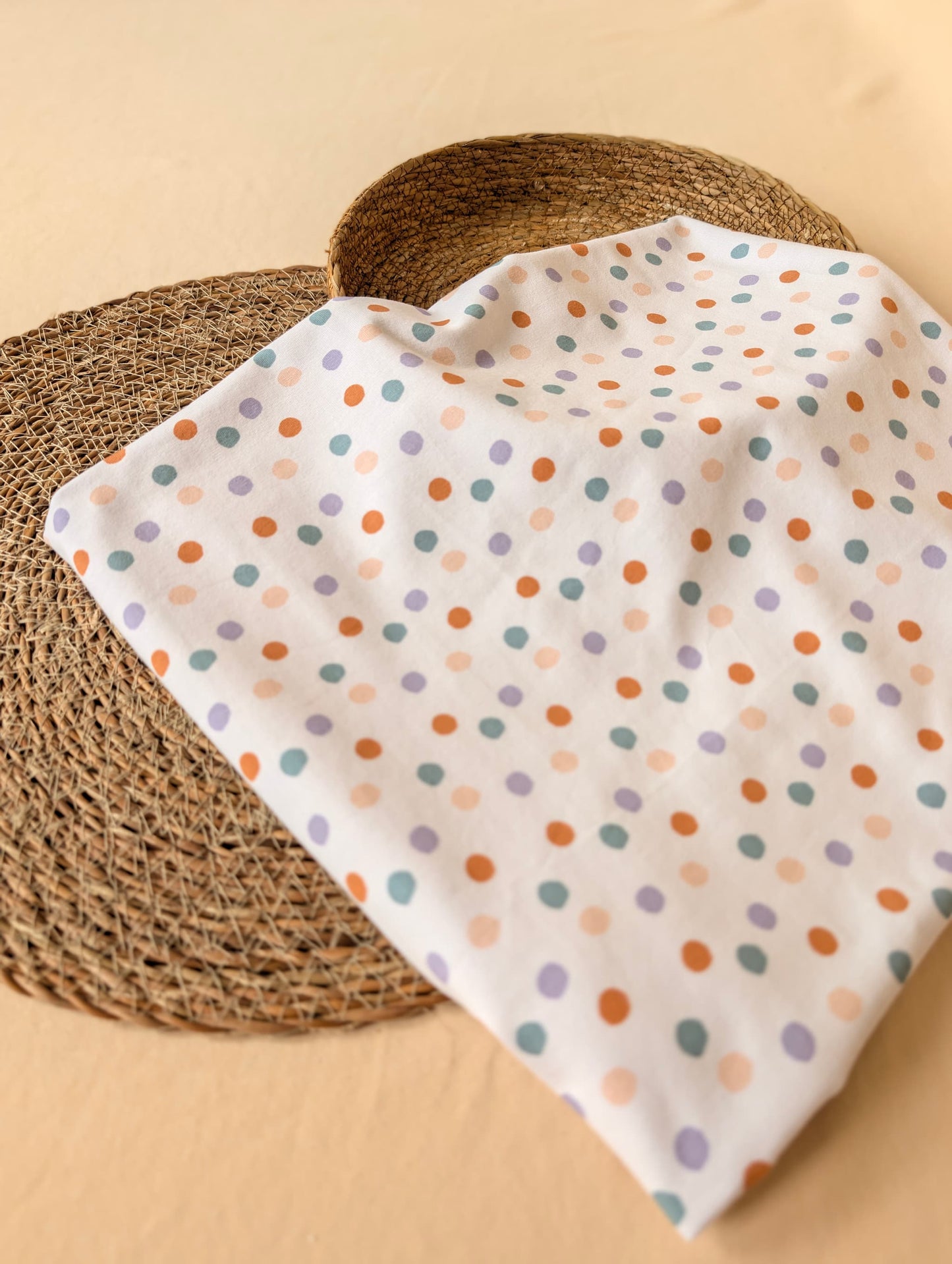 Cotton jersey fabric folded on a rattan placemat — Etta Spot pastel multi scattered spot print on white