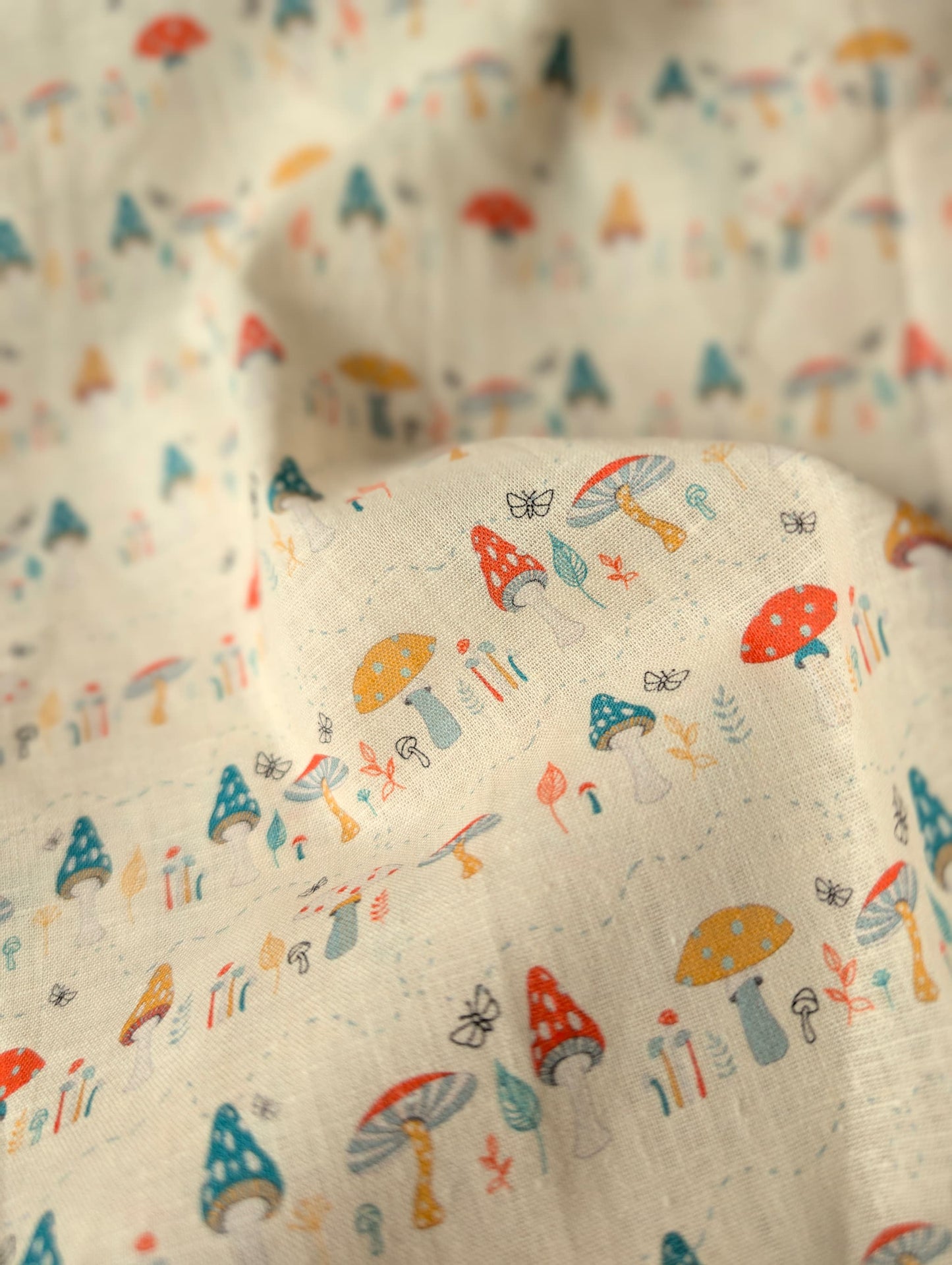 Close-up of linen cotton fabric draped and gathered — Hazel Woodland print showing individual toadstool varieties and botanical motifs in rich colour on natural