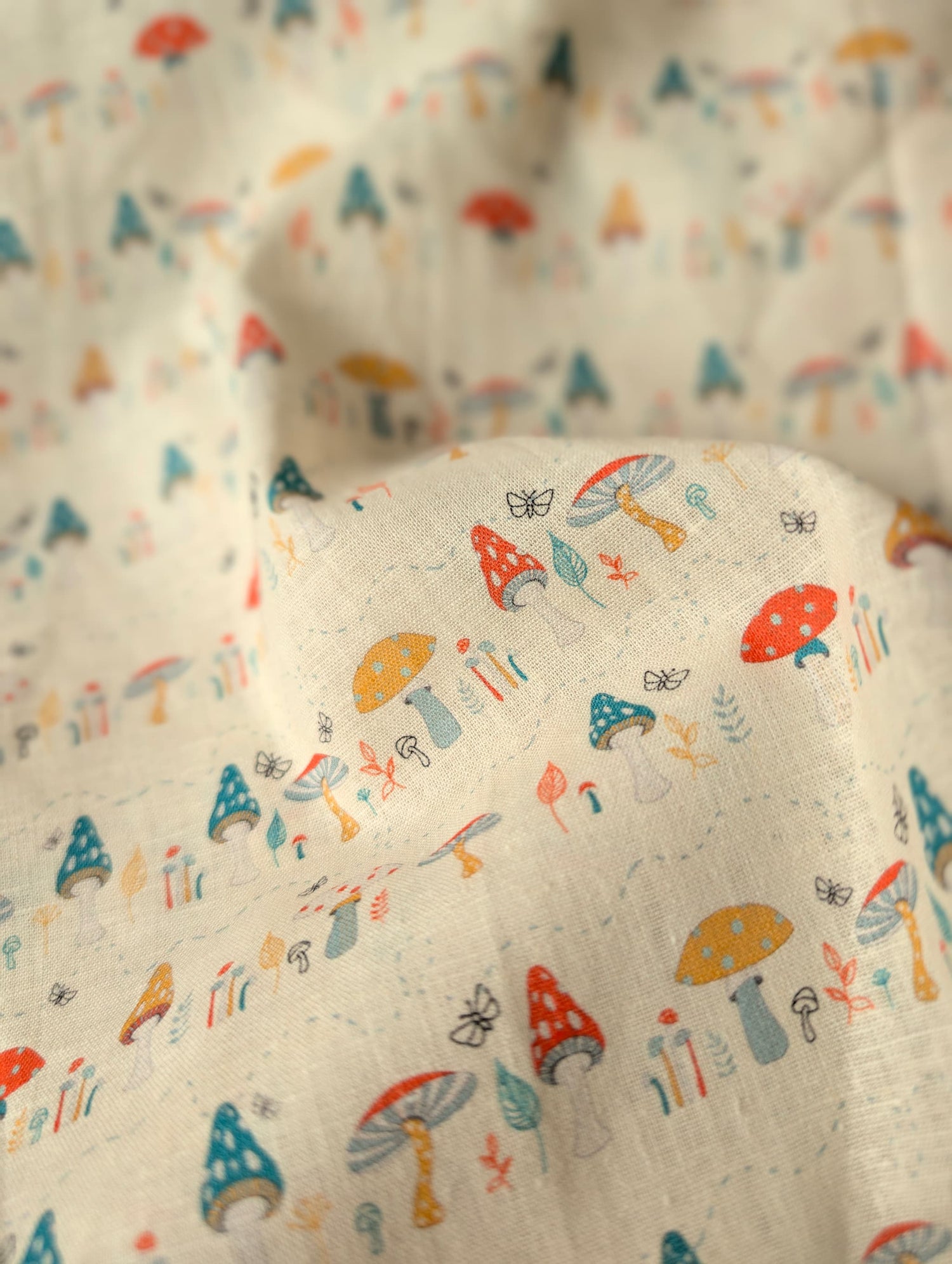 Close-up of linen cotton fabric draped and gathered — Hazel Woodland print showing individual toadstool varieties and botanical motifs in rich colour on natural