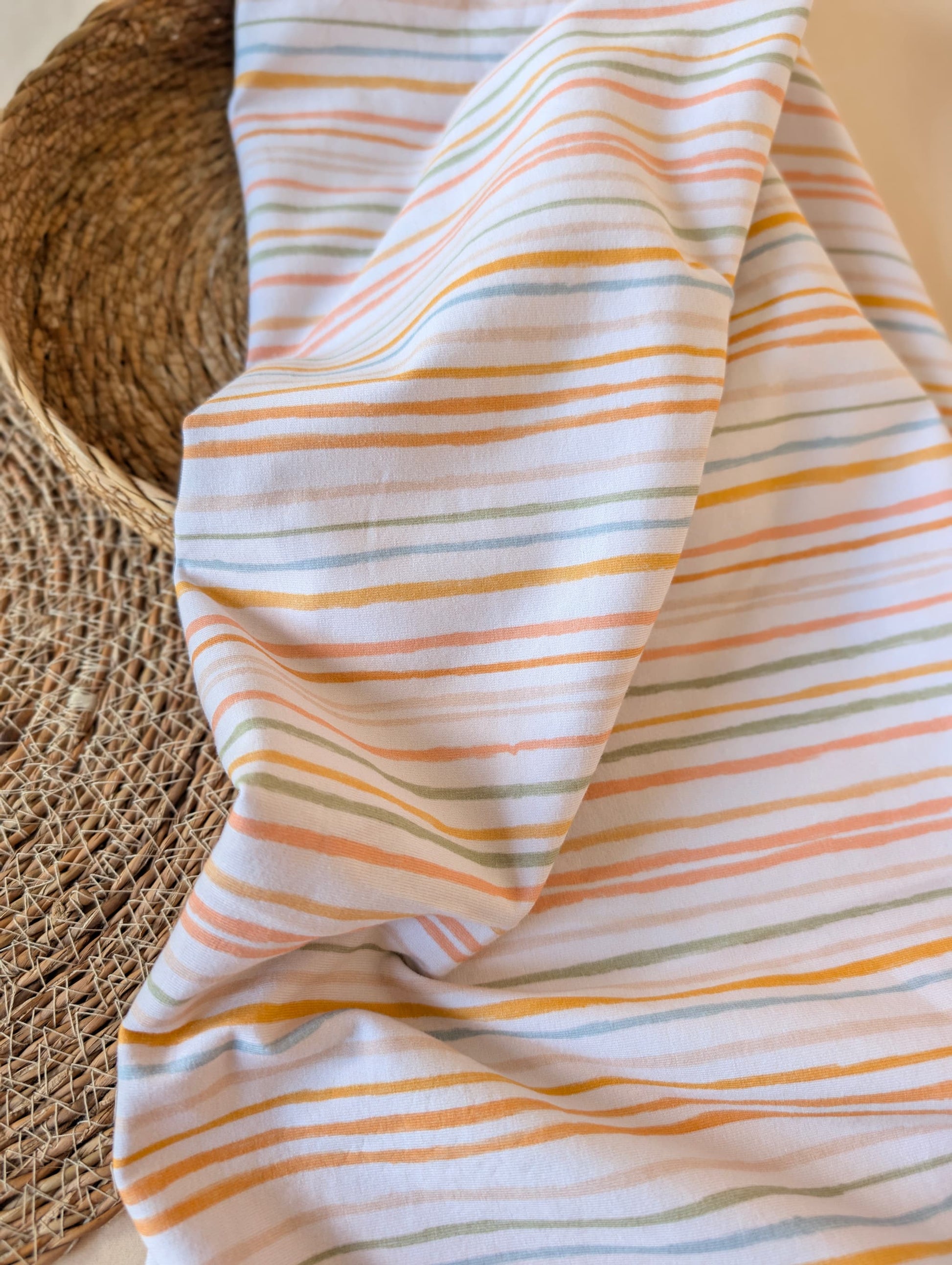 Cotton jersey fabric draped over a rattan chair showing drape and stretch — Isla Stripe pastel multi striped cotton jersey
