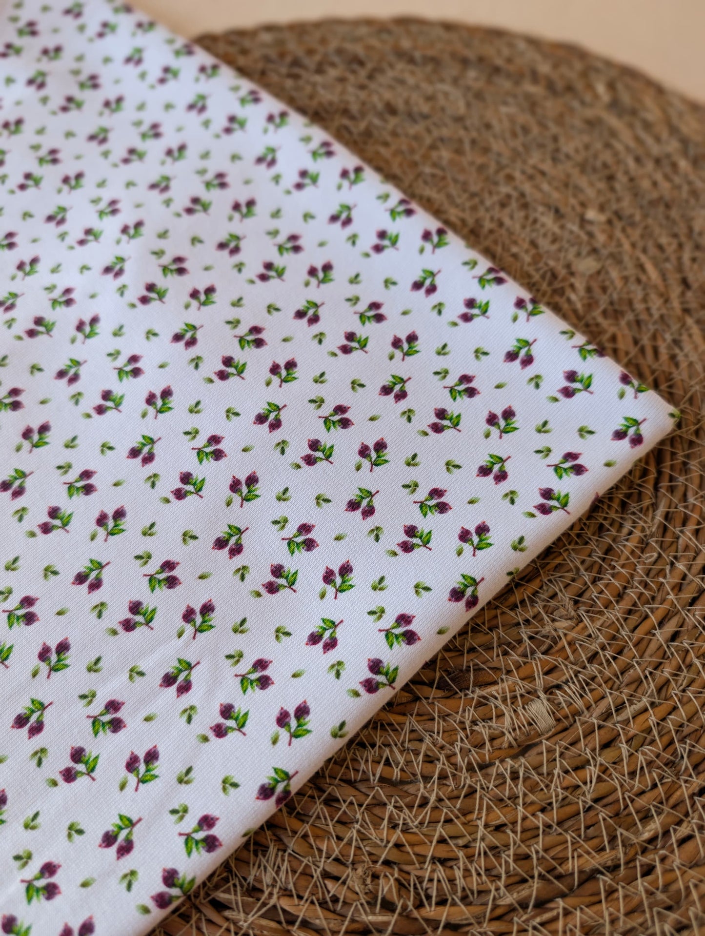 Cotton rib fabric folded on a rattan placemat — Mini Blueberries, plum berry clusters and green leaves on white cotton rib