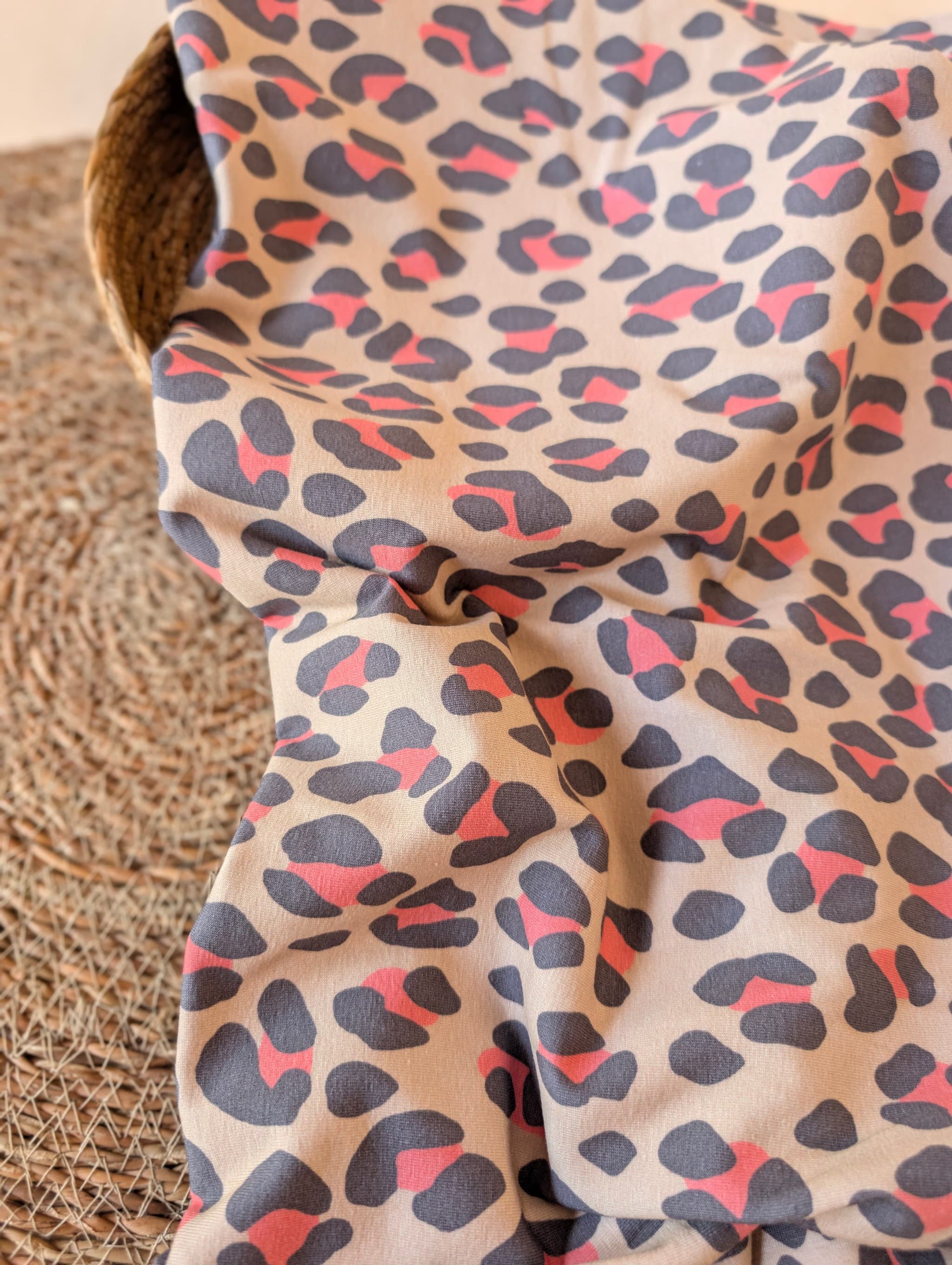 Nala Animal Print cotton jersey draped over a wicker basket showing the soft drape and generous 160cm width — slate and coral leopard print by Esorai