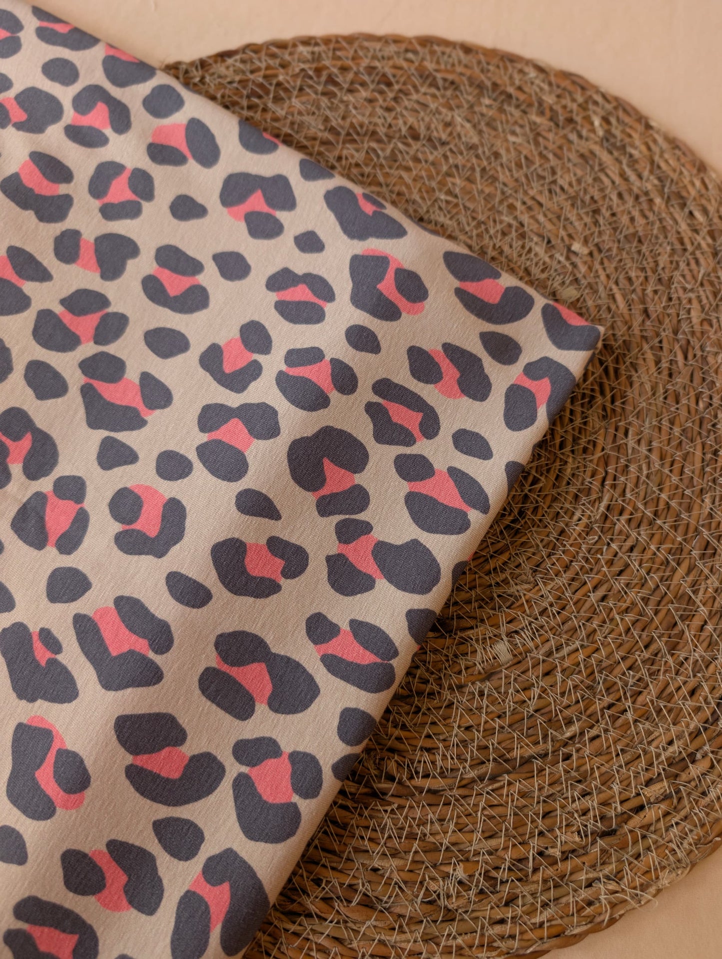 Nala Animal Print cotton jersey folded on a wicker mat, bold slate and coral leopard spots on a warm natural ground — Esorai