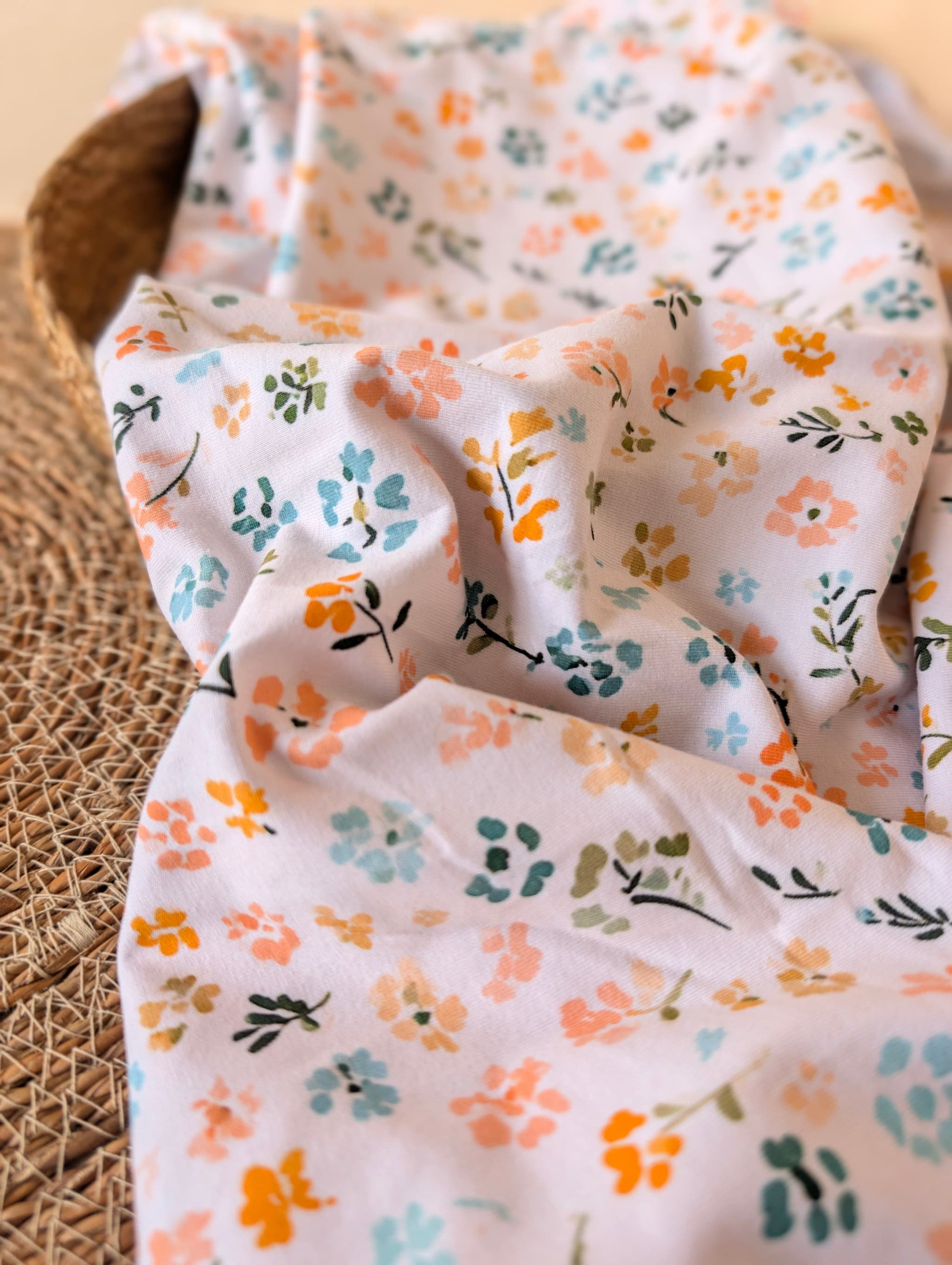 Close-up of cotton jersey fabric showing painterly ditsy florals — Nell Floral in peach, mustard, teal and sage on white