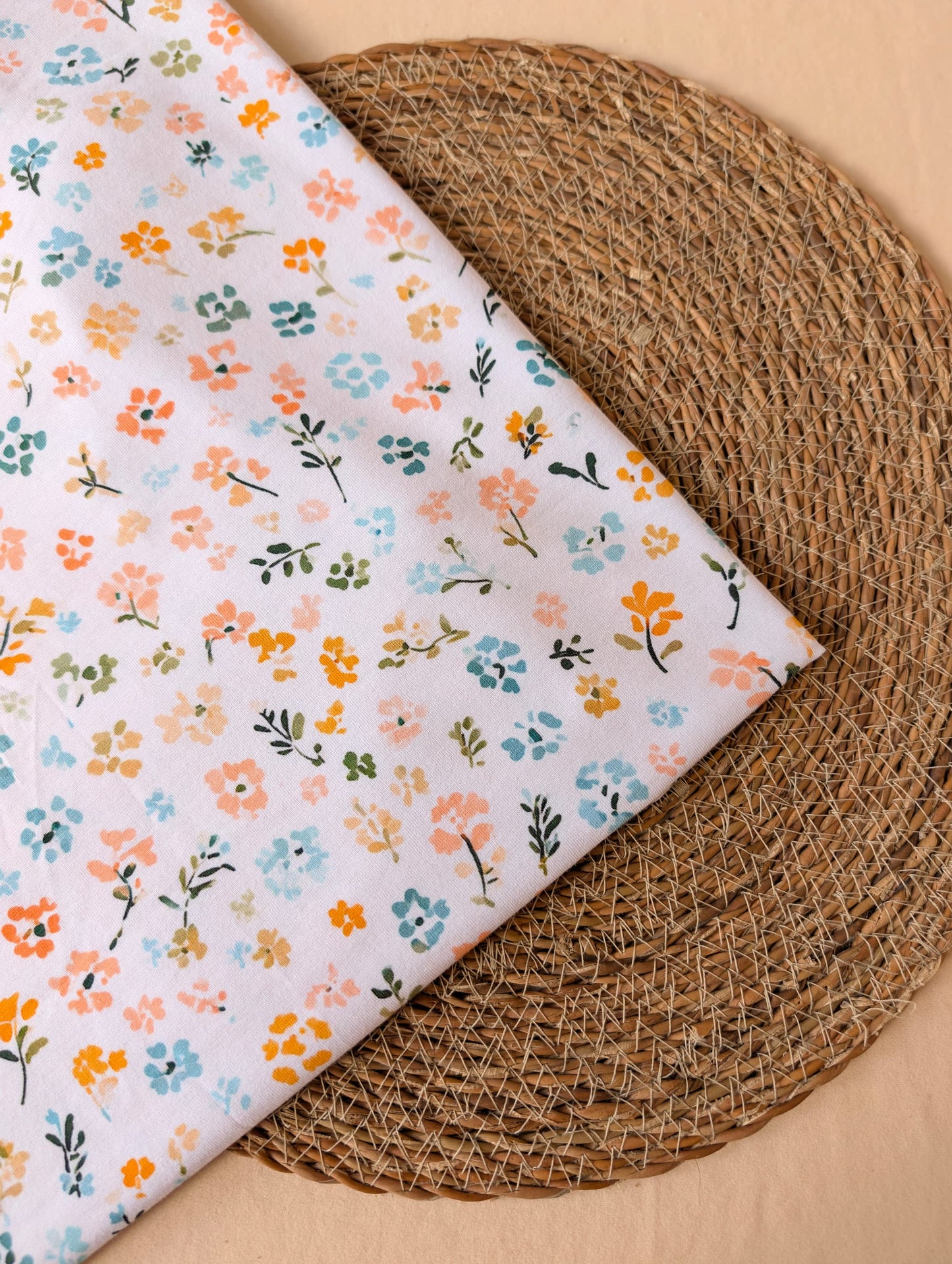 Cotton jersey fabric folded on a rattan placemat — Nell Floral pastel multi ditsy floral print on white cotton jersey