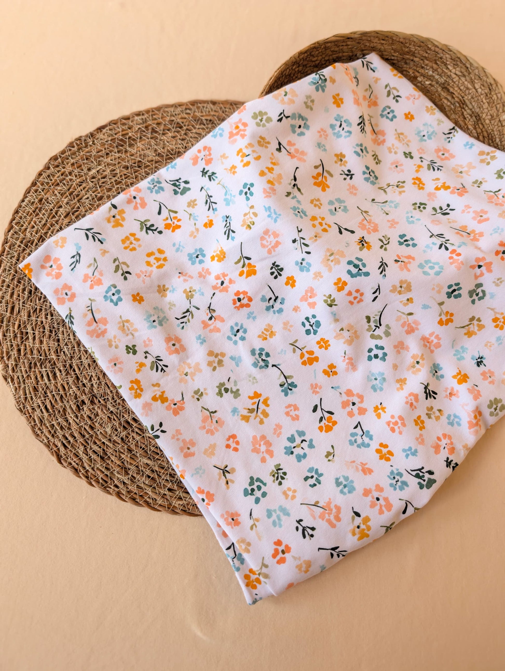 Cotton jersey Nell Floral fabric laid flat on a rattan placemat showing the full scattered floral print in pastel multi
