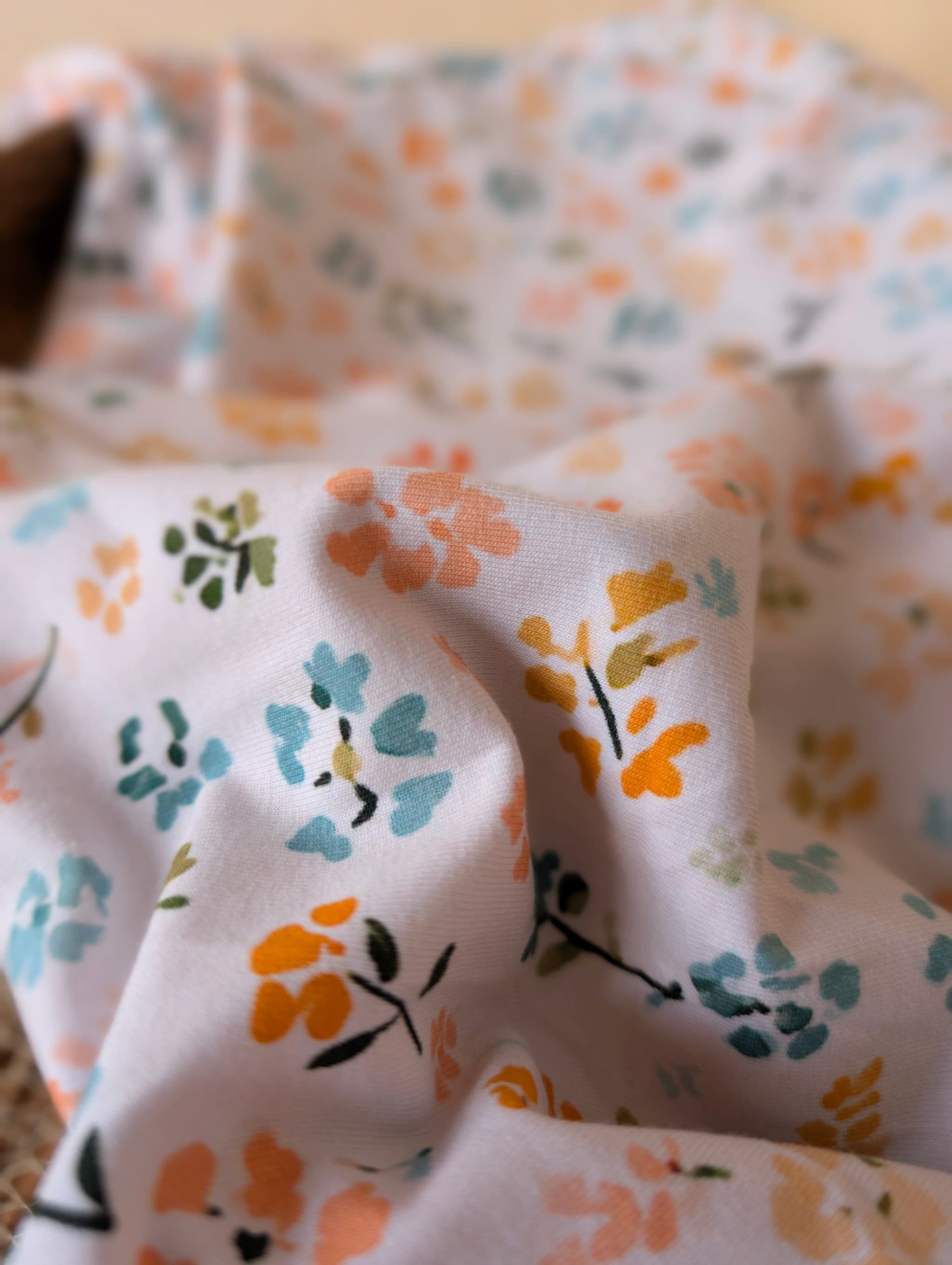 Cotton jersey fabric draped in a rattan basket showing drape and stretch — Nell Floral pastel multi ditsy floral cotton jersey