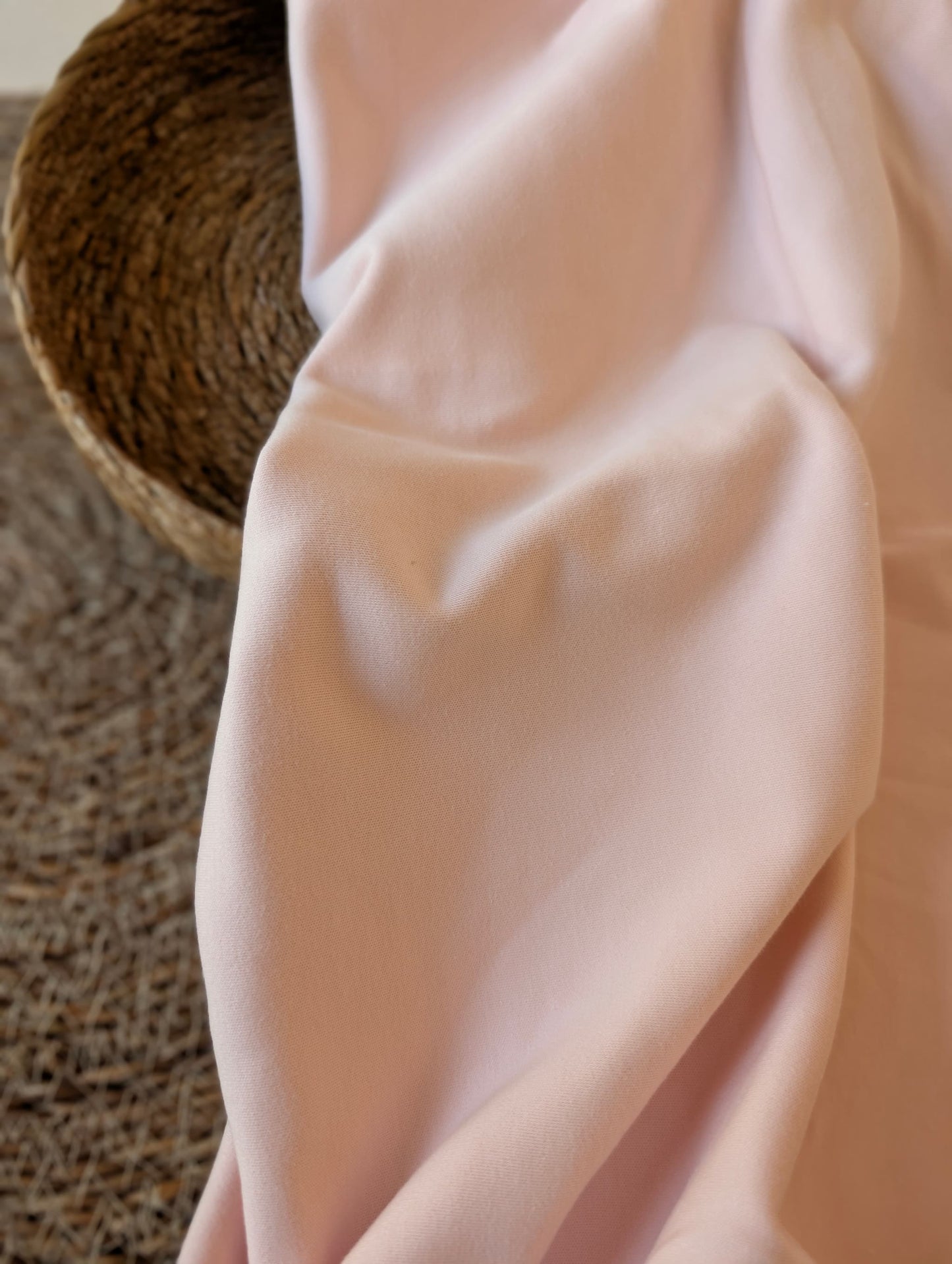 Pale blush pink premium-weight organic cotton jersey draped over a wicker basket — Cotton Jersey Plain in Blush by Esorai