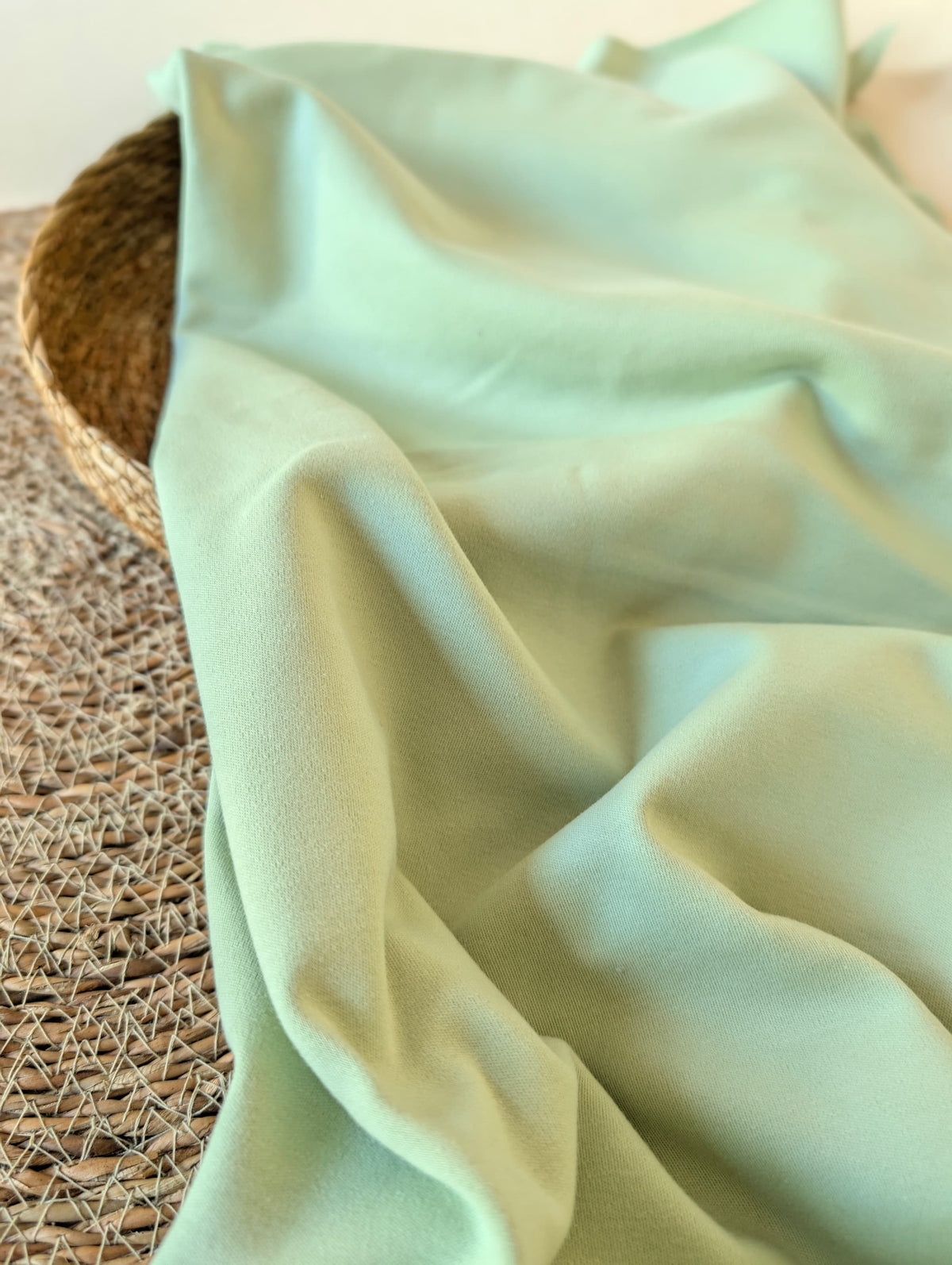 Soft mint green premium-weight organic cotton jersey draped over a wicker basket — Cotton Jersey Plain in Pistachio by Esorai