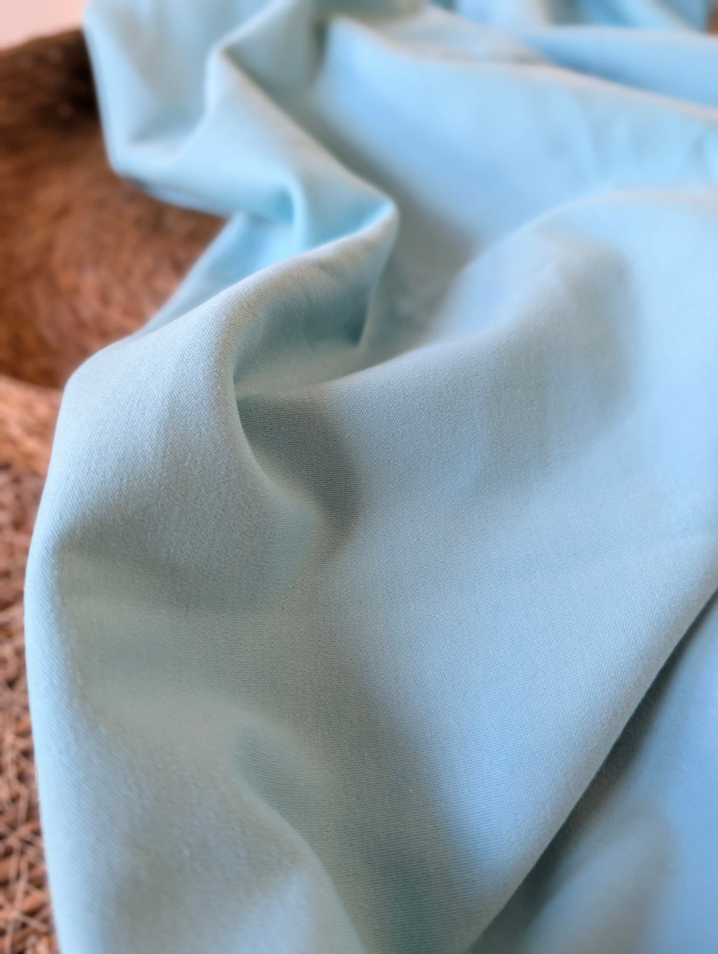 Pale powder blue premium-weight organic cotton jersey draped over a wicker basket — Cotton Jersey Plain in Powder by Esorai