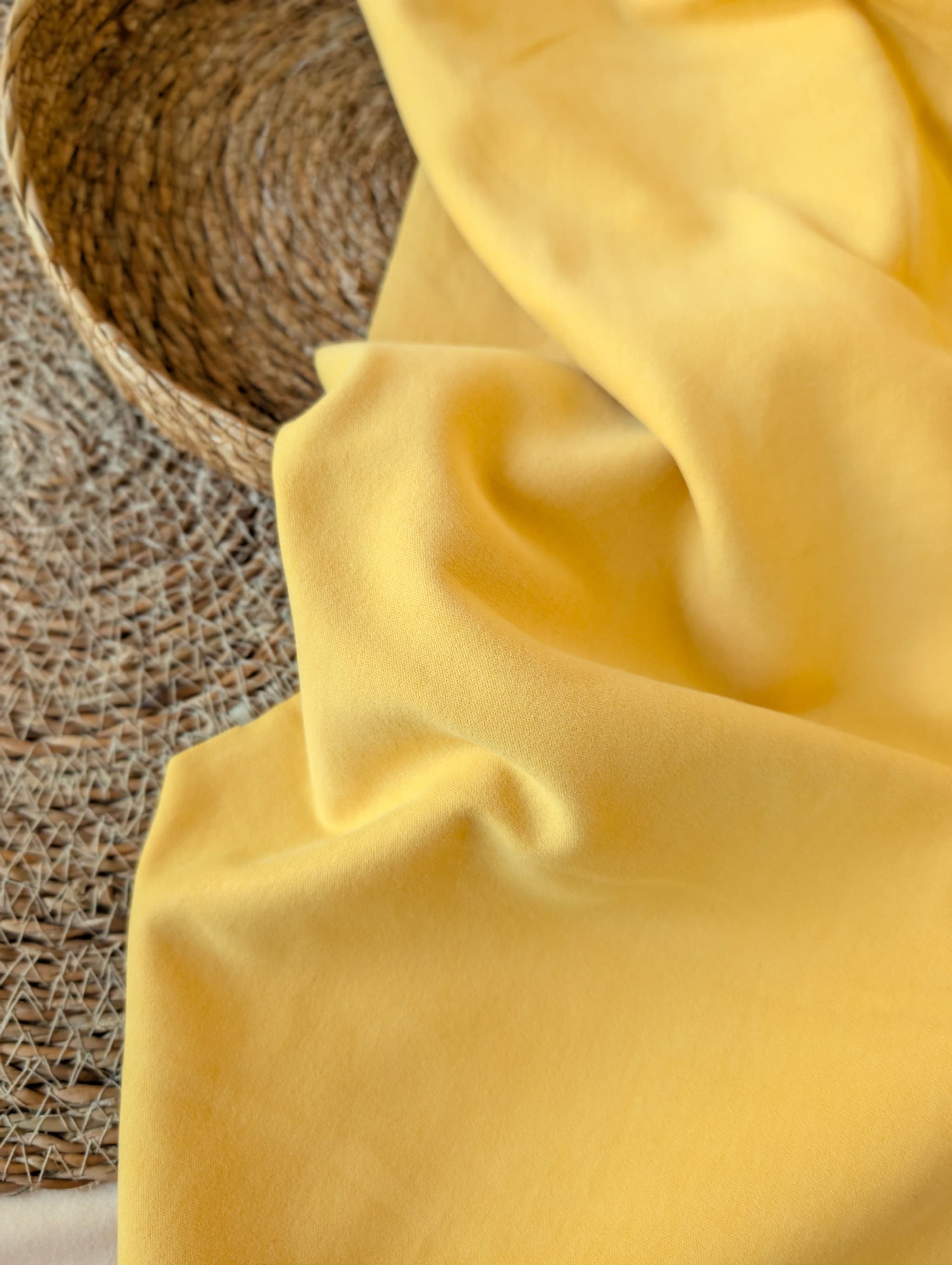 Warm yellow premium-weight organic cotton jersey draped over a wicker basket — Cotton Jersey Plain in Buttercup by Esorai
