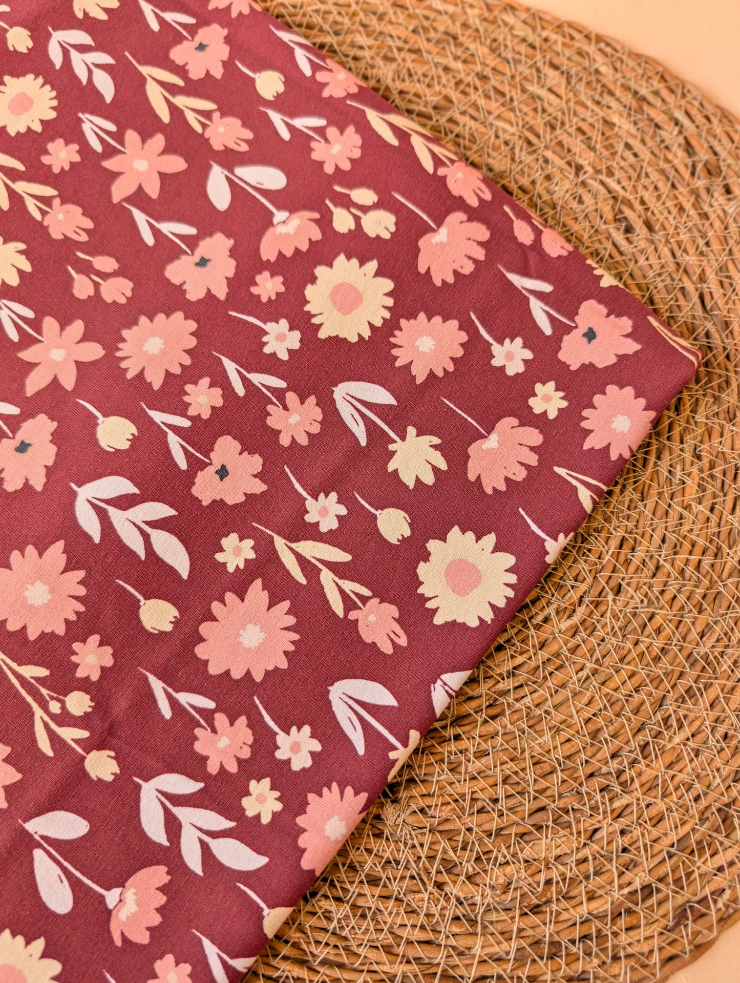 Ottie Floral cotton jersey folded flat on wicker showing the full print detail — scattered flowers and leaves in pink, blush and cream on burgundy — Esorai