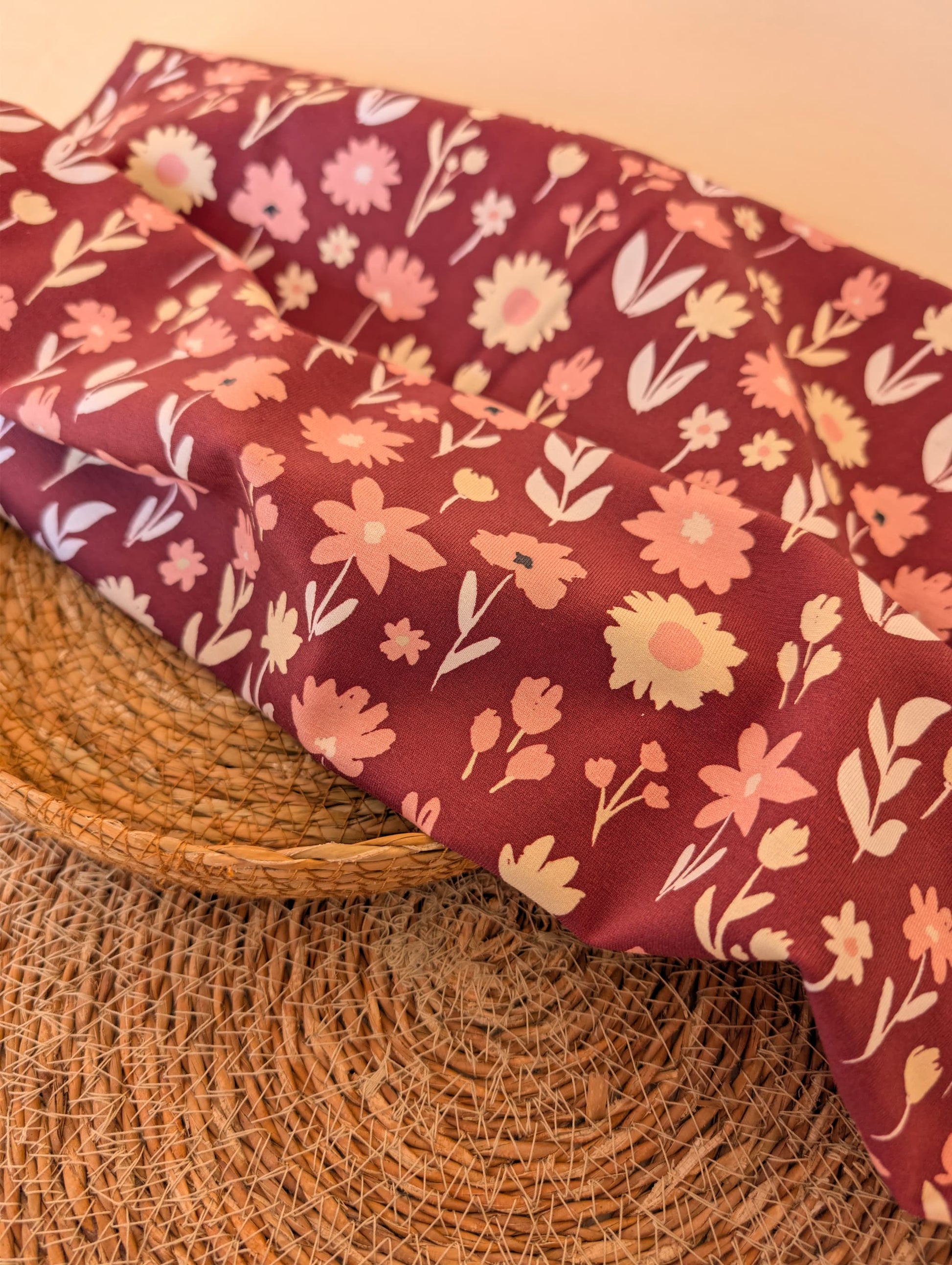 Ottie Floral cotton jersey draped over a wicker basket — scattered daisy and tulip print in pink and cream on a deep burgundy ground — Esorai