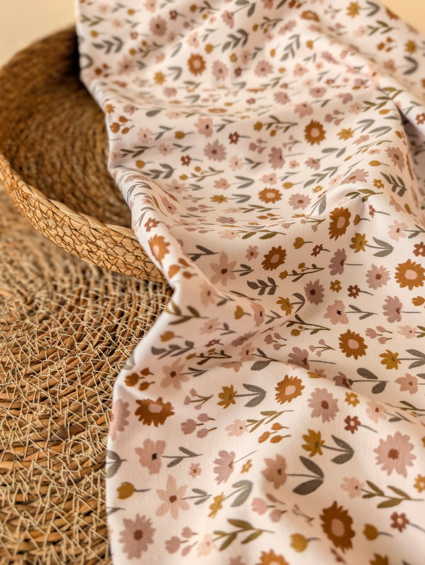 Ottie Floral cotton jersey in Ivory draped over a wicker basket showing the soft drape and meadow wildflower print — Esorai