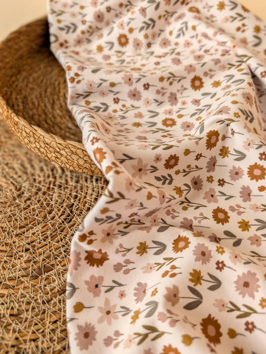 Ottie Floral cotton jersey in Ivory draped over a wicker basket showing the soft drape and meadow wildflower print — Esorai