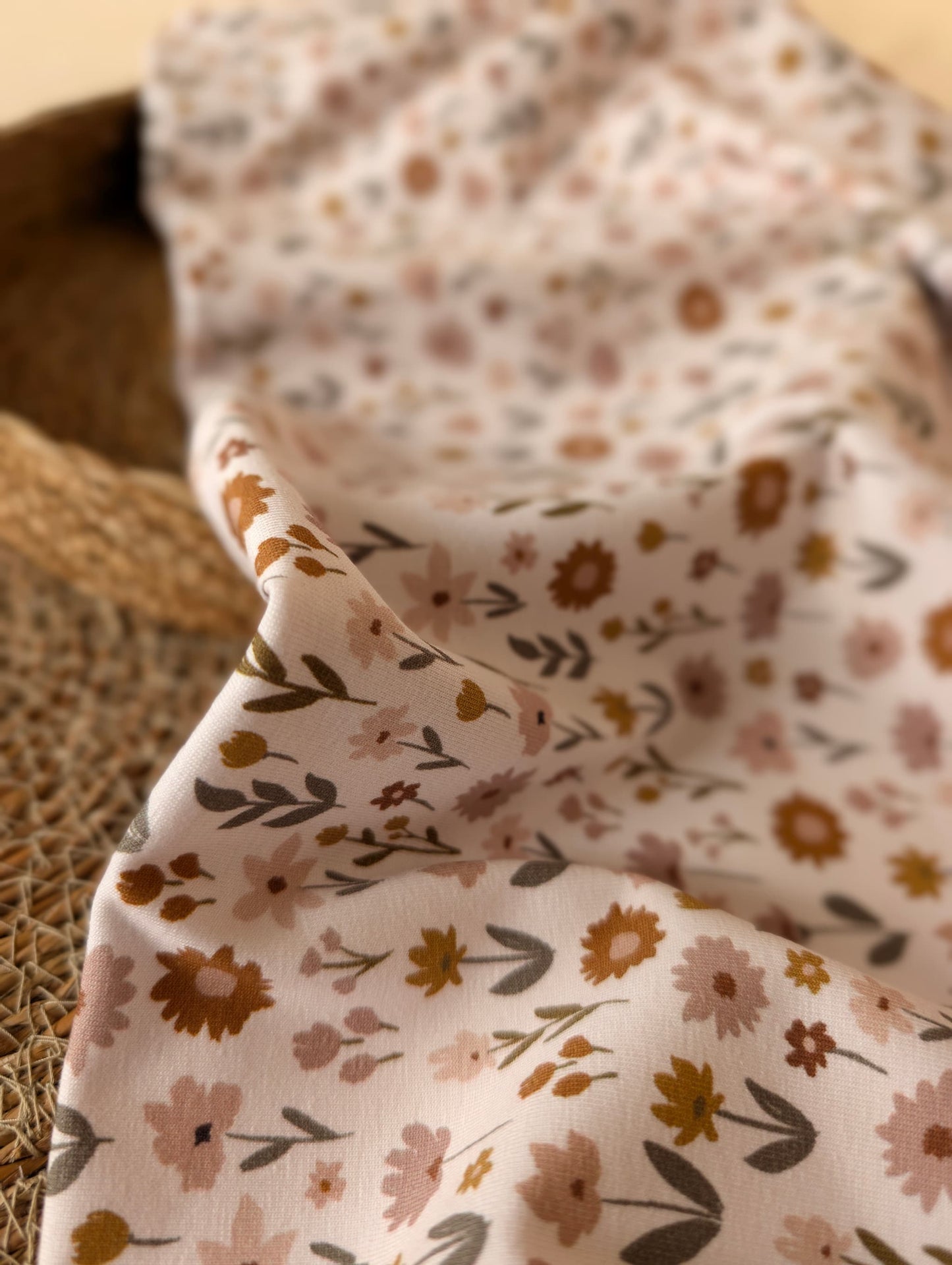 Close-up of Ottie Floral cotton jersey showing print detail — scattered daisies, sunflowers and sprigs in dusty pink, mustard and rust on an ivory ground — Esorai