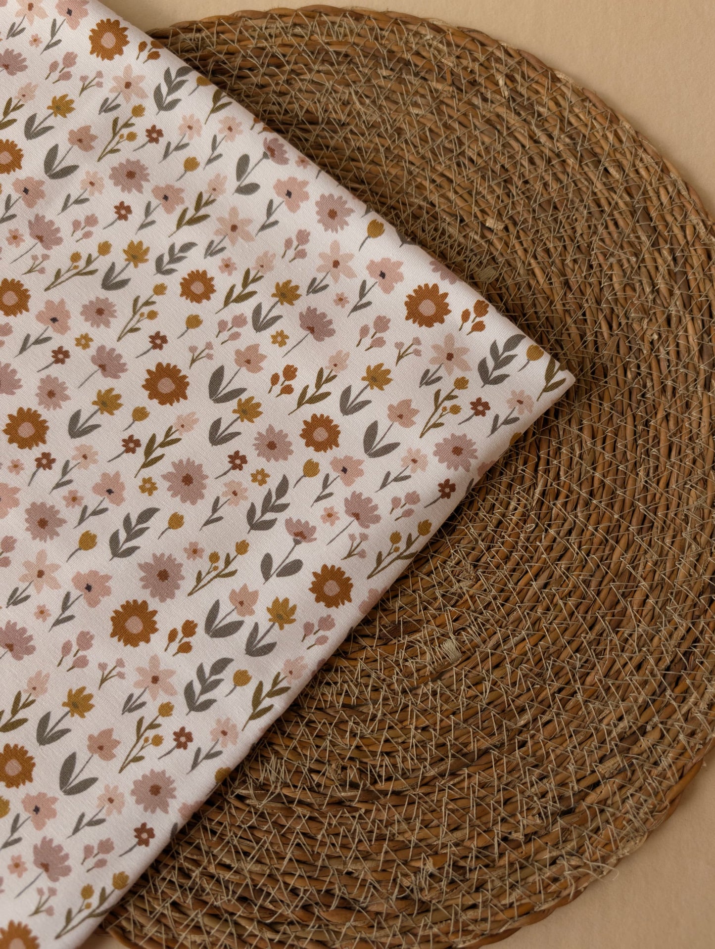 Ottie Floral cotton jersey in Ivory folded on a wicker mat — earthy meadow wildflower print in dusty pink, mustard and sage — Esorai