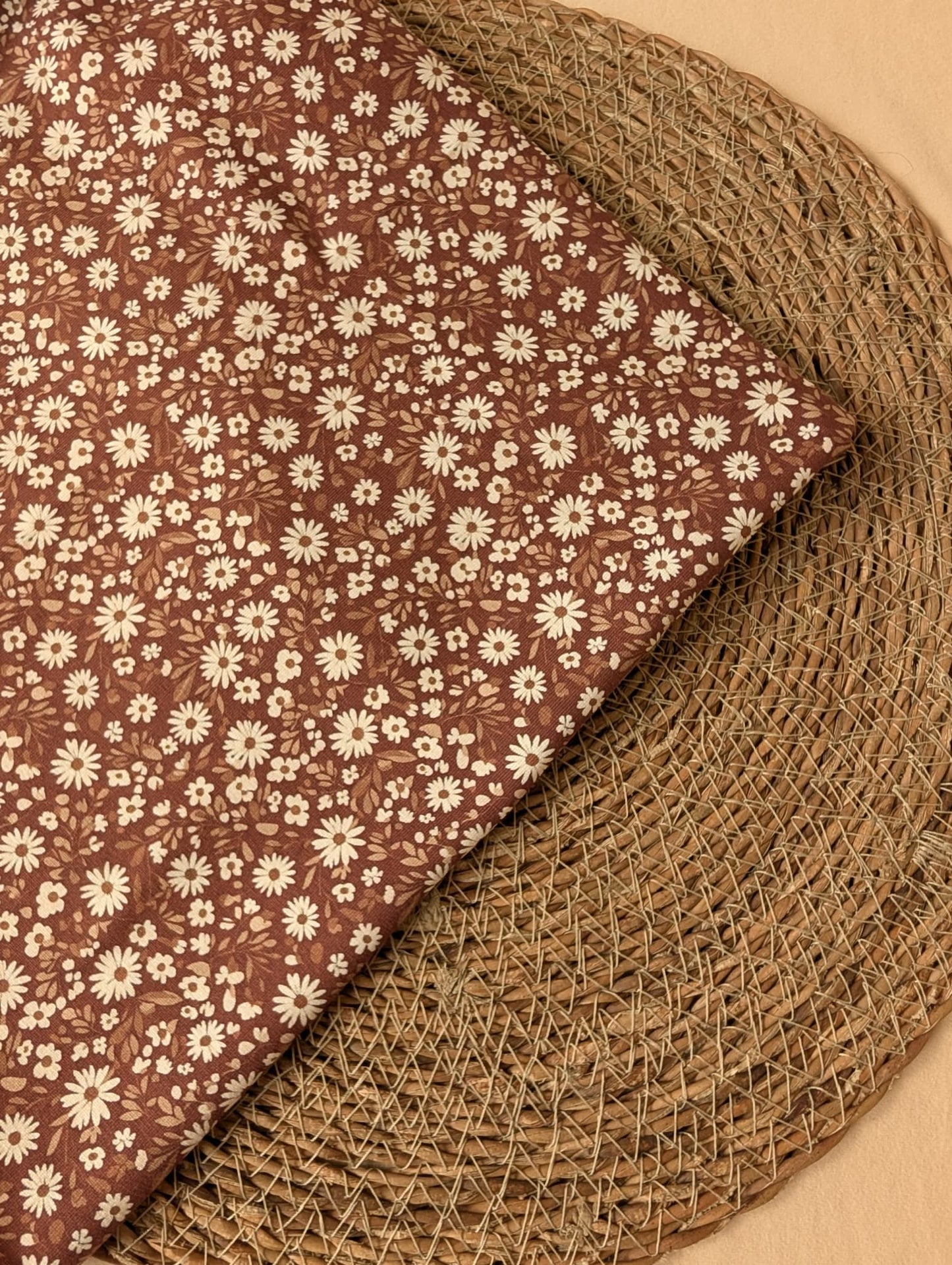 Willa Floral Cotton Jersey Rust — folded corner detail of white daisy print on warm brown jersey, on woven rattan placemat