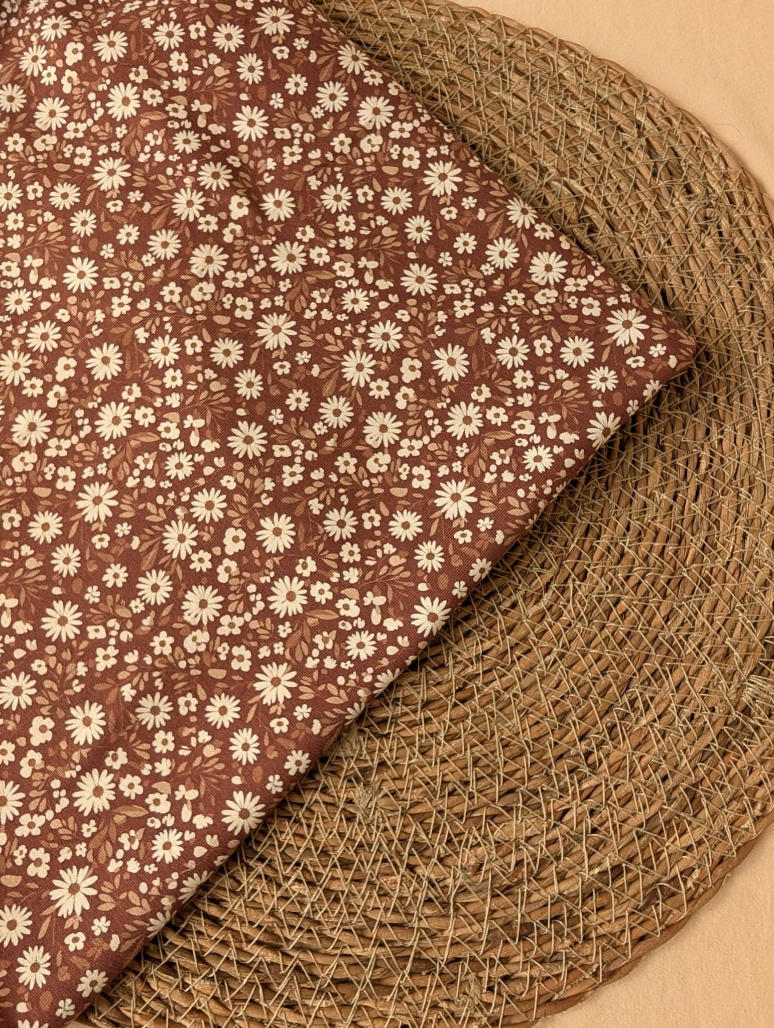 Willa Floral Cotton Jersey Rust — folded corner detail of white daisy print on warm brown jersey, on woven rattan placemat