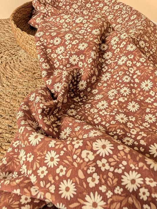 Willa Floral Cotton Jersey Rust — draped fabric showing soft stretch and all-over ditsy daisy print with cream flowers and tan leaves on chocolate brown ground