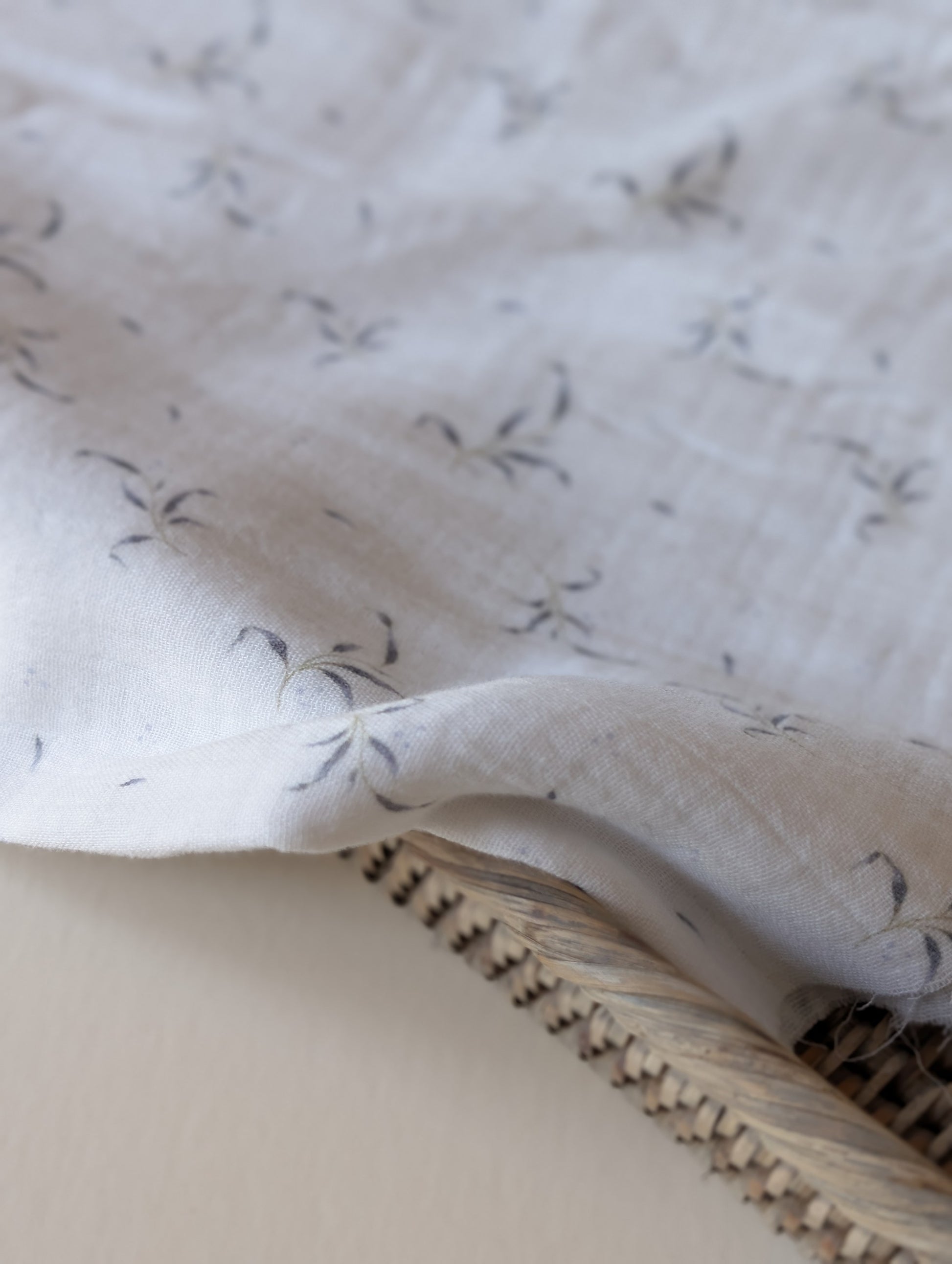 Close-up of double gauze fabric folded over a rattan basket edge showing Winnie leaf sprig print detail and soft crinkle texture