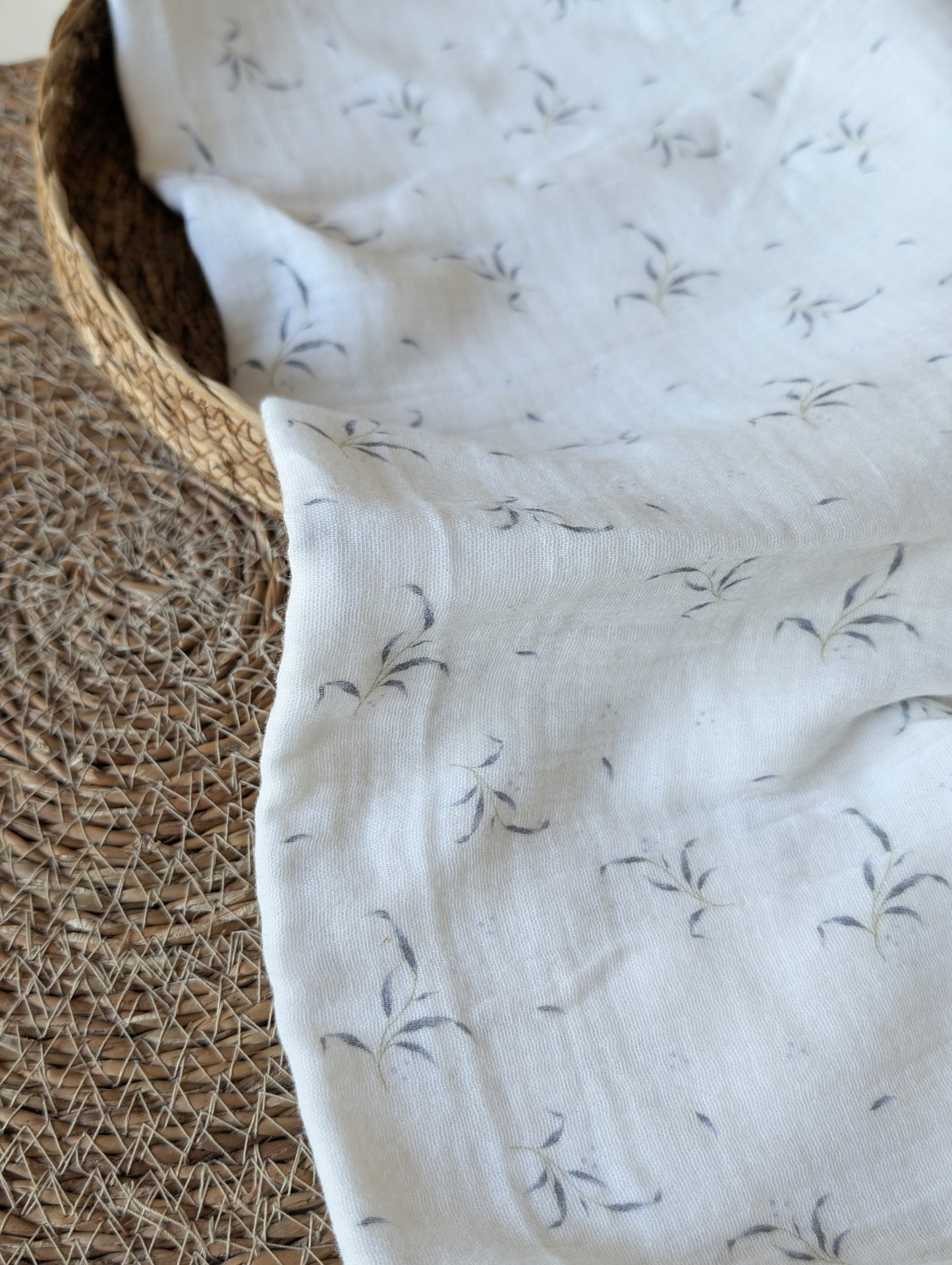 Winnie double gauze fabric folded in a rattan basket on a plain background showing soft drape and leaf sprig print