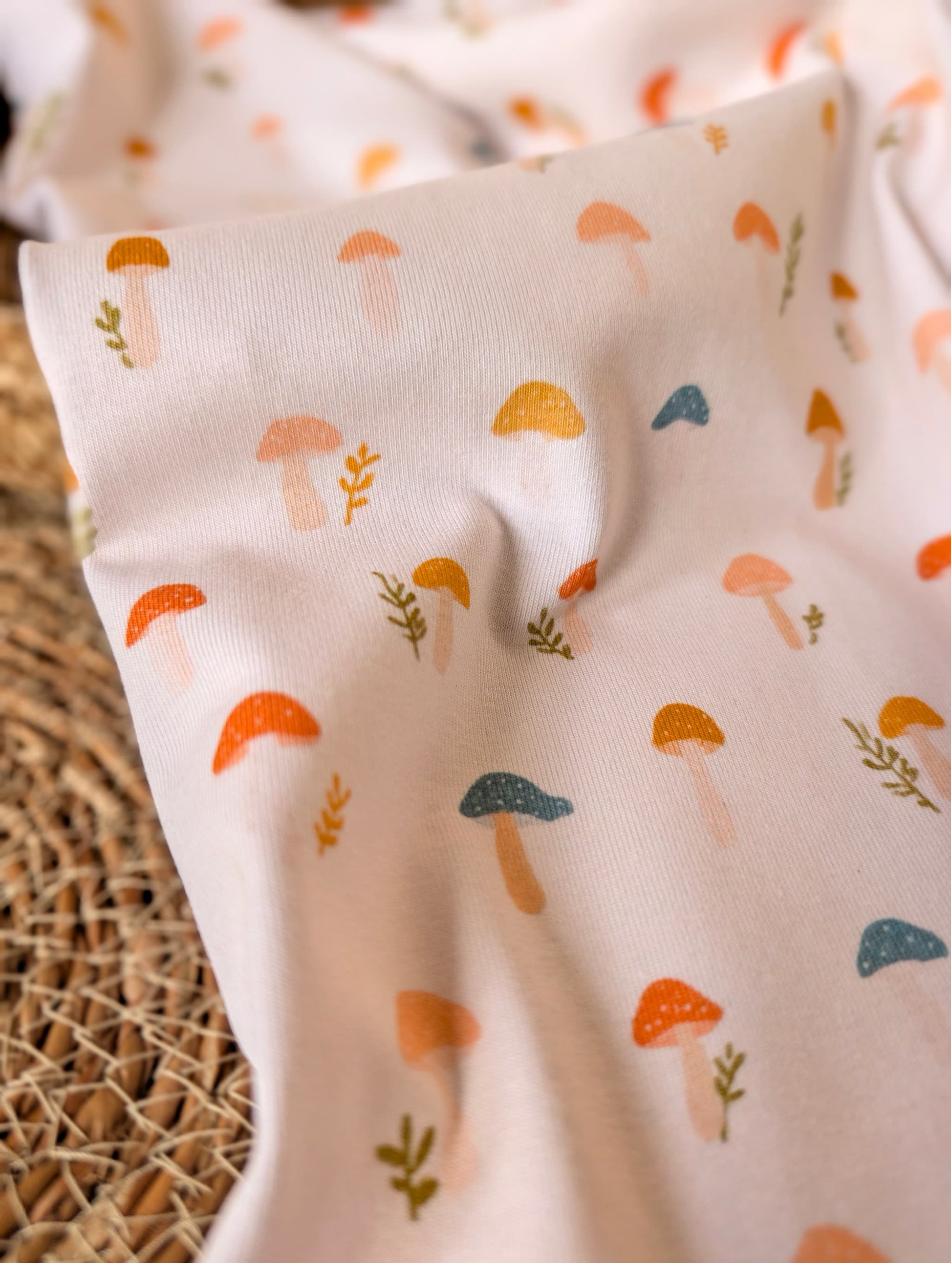 Cotton rib fabric draped on rattan showing scattered toadstool and botanical print — Wren in terracotta, mustard, teal and peach on white